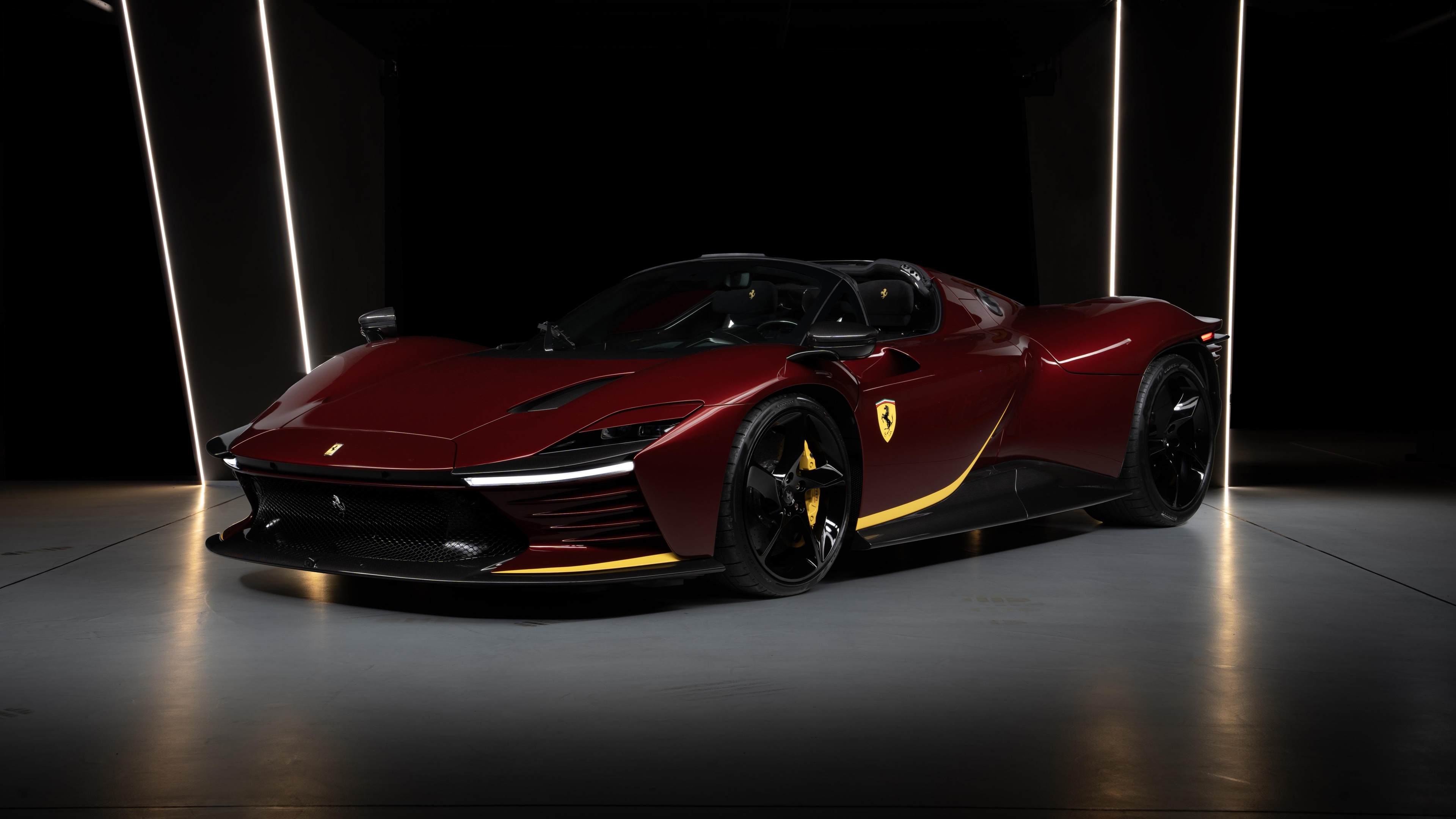 A high-resolution close-up of a maroon Ferrari Daytona SP3 sports car against a dark, minimalist background.