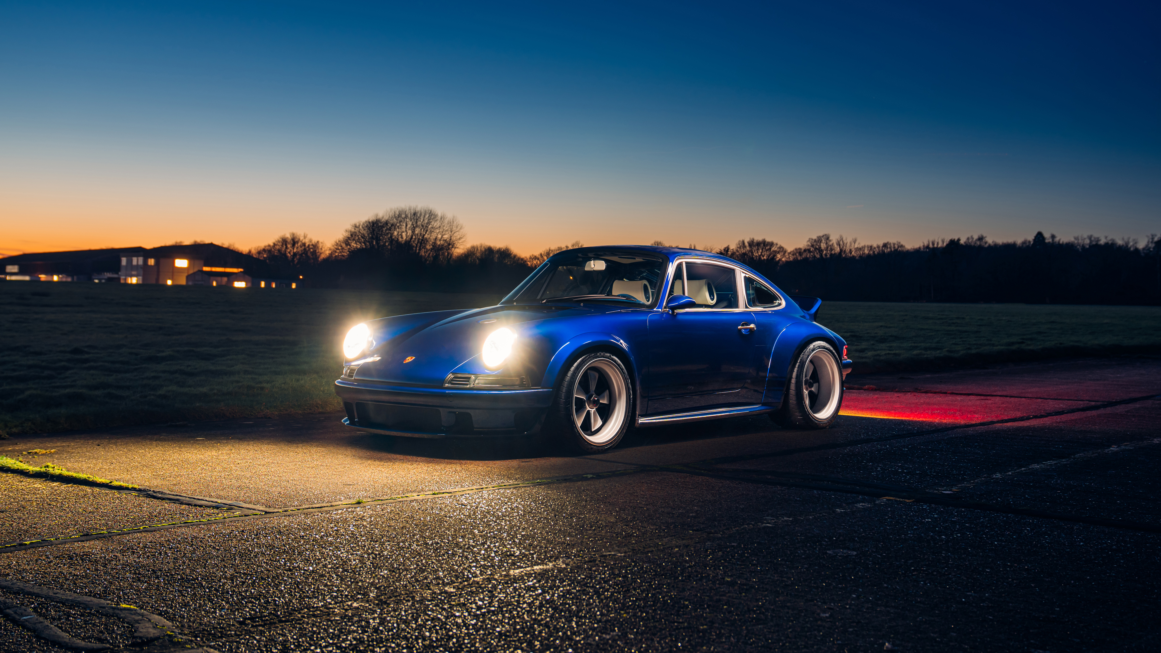 A classic Porsche 911 parked under a beautiful orange and yellow sunset sky.