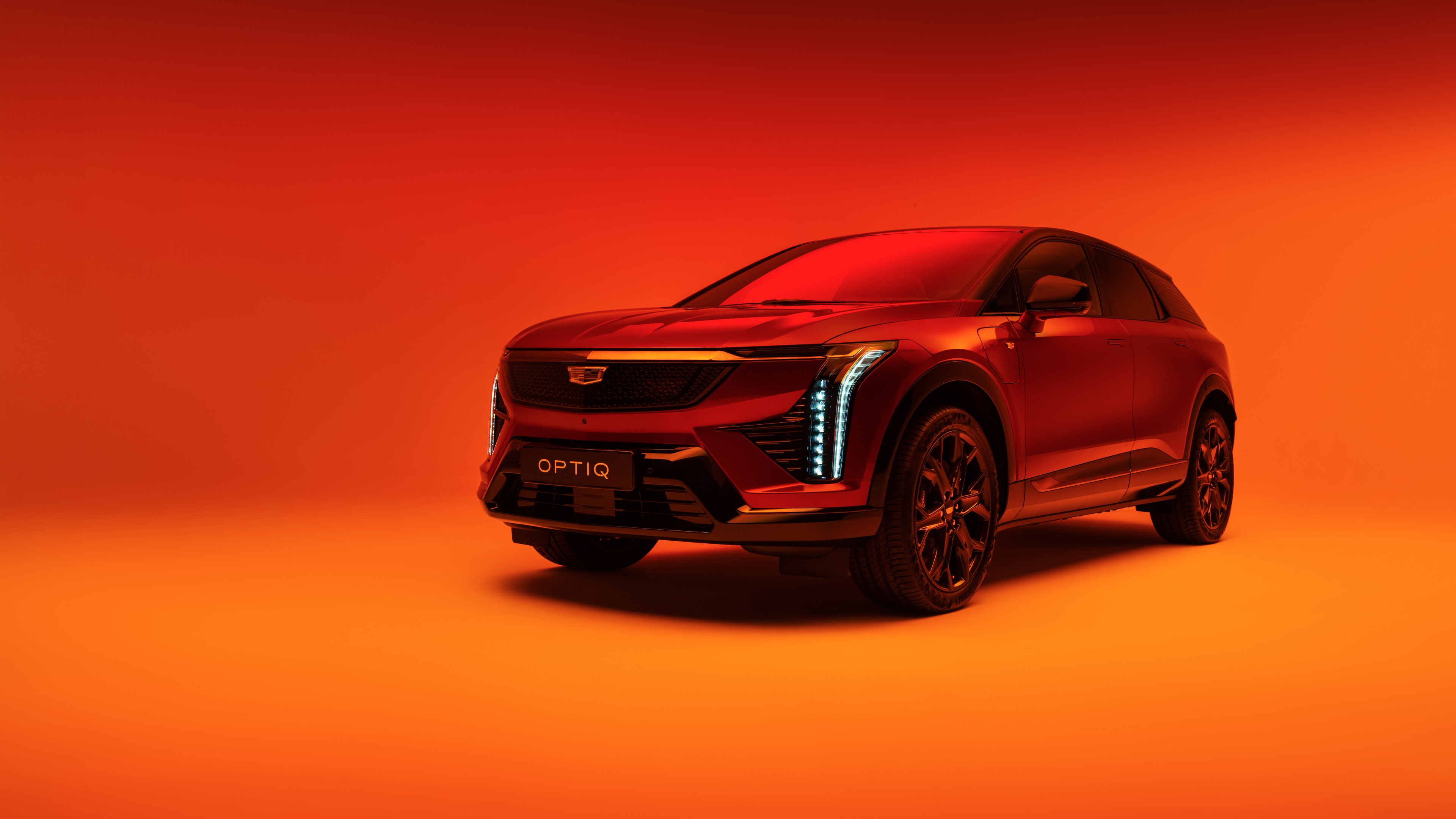 The 2025 Cadillac Optiq electric SUV presented against a bold orange background.