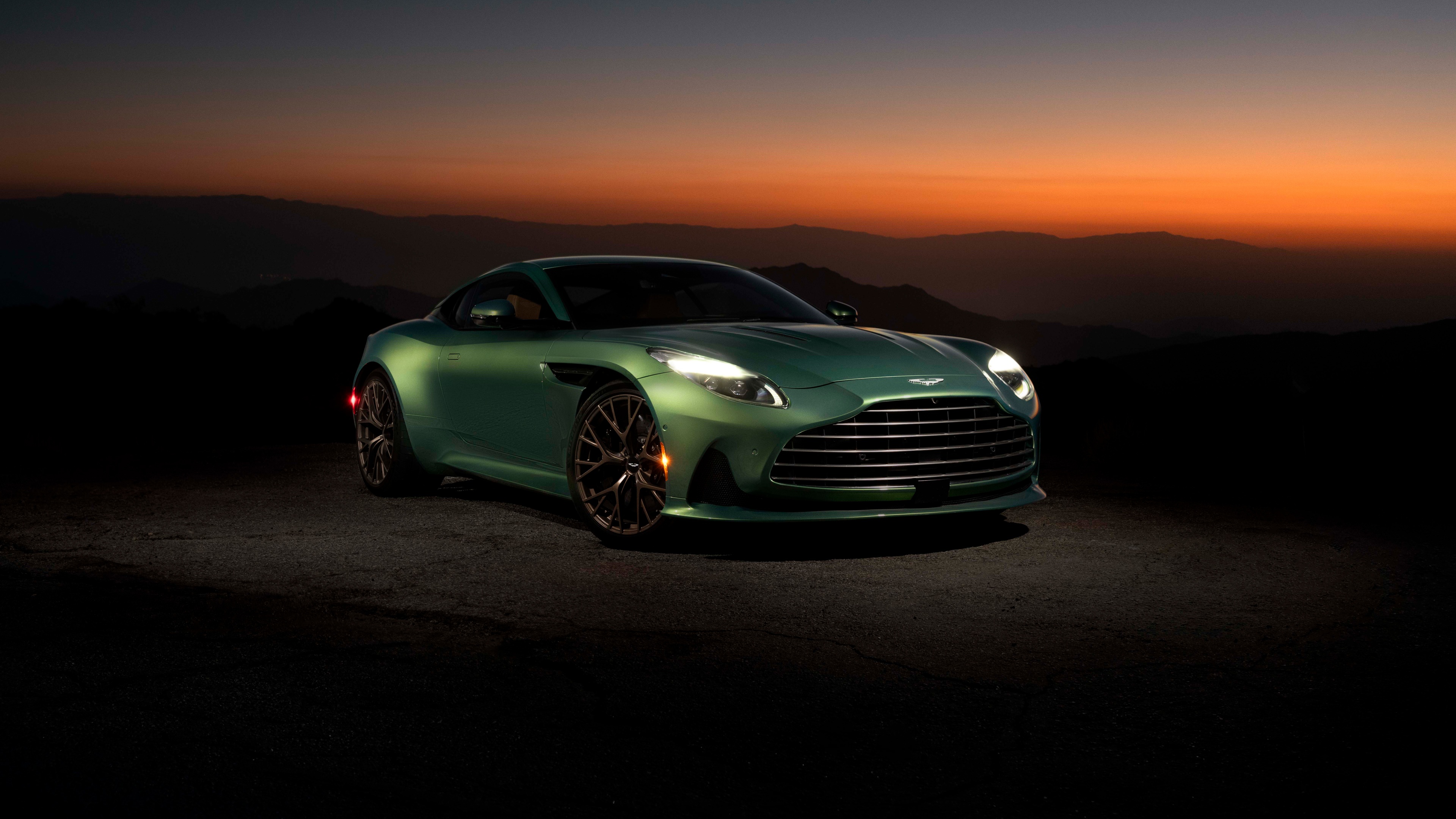A sleek Aston Martin DB12 supercar positioned against a dramatic and colorful sunset sky.