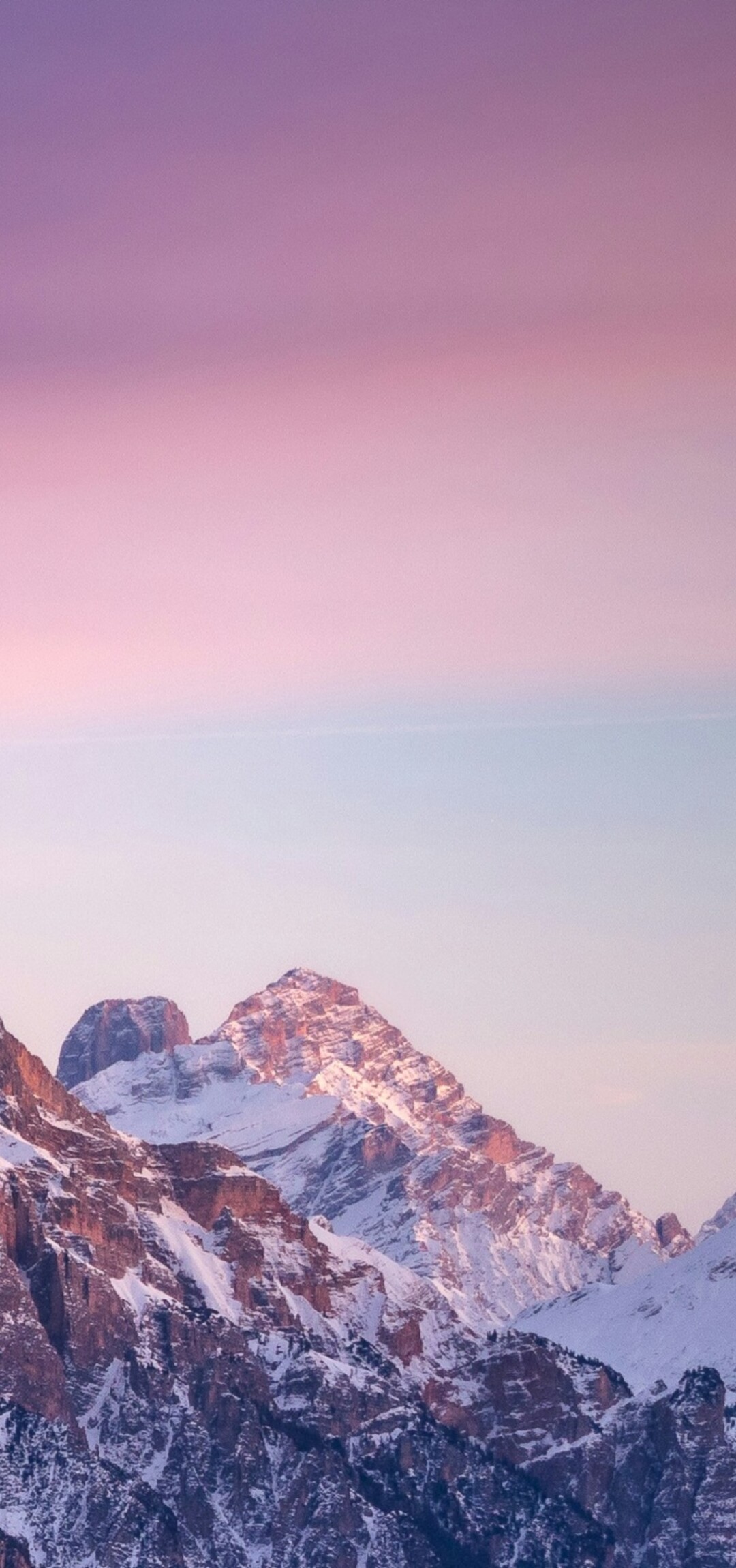 A panoramic view of snow-covered mountains at sunset with a colorful gradient sky and golden hour lighting.
