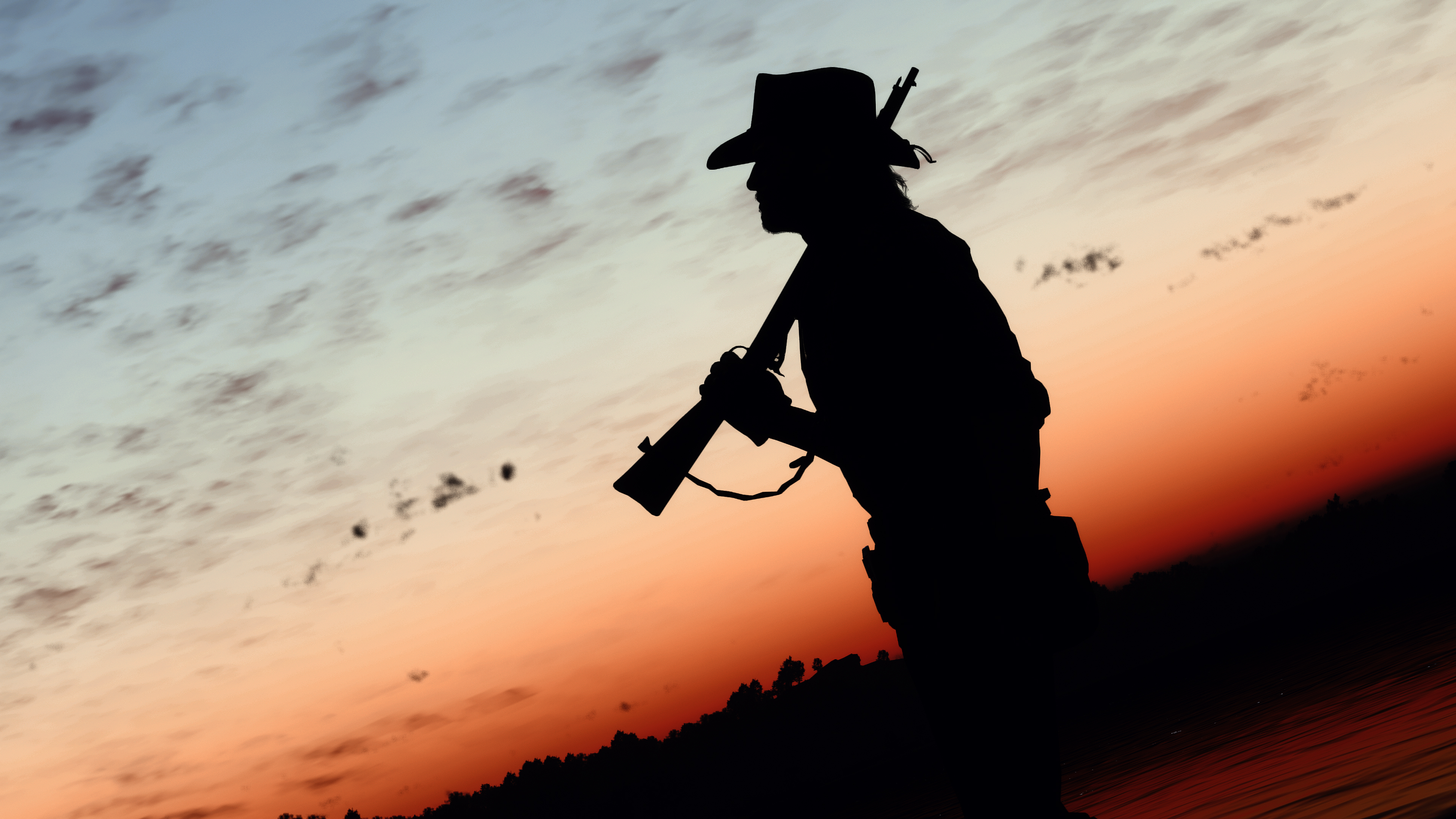 A silhouette of a lone cowboy standing against a large, glowing orange and red sunset in a Western landscape.