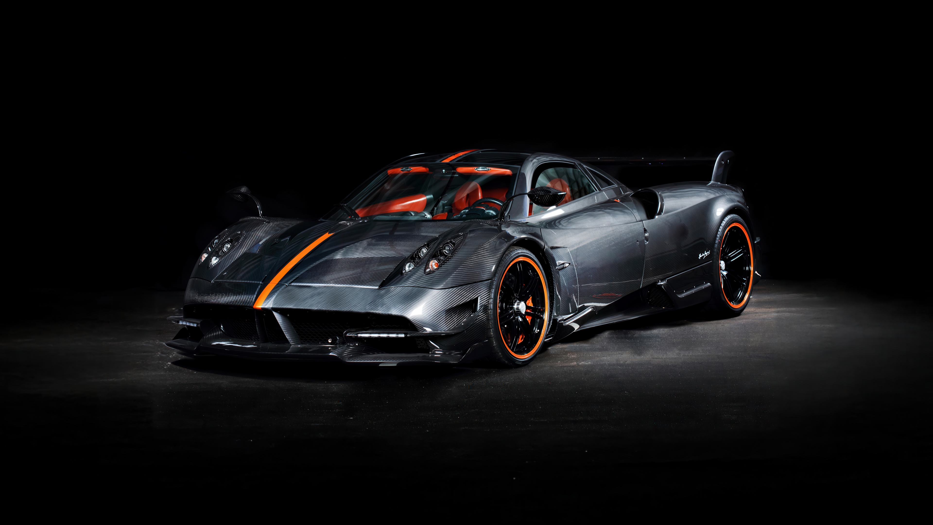 A sleek black hypercar with visible carbon fiber details against a dark black background.
