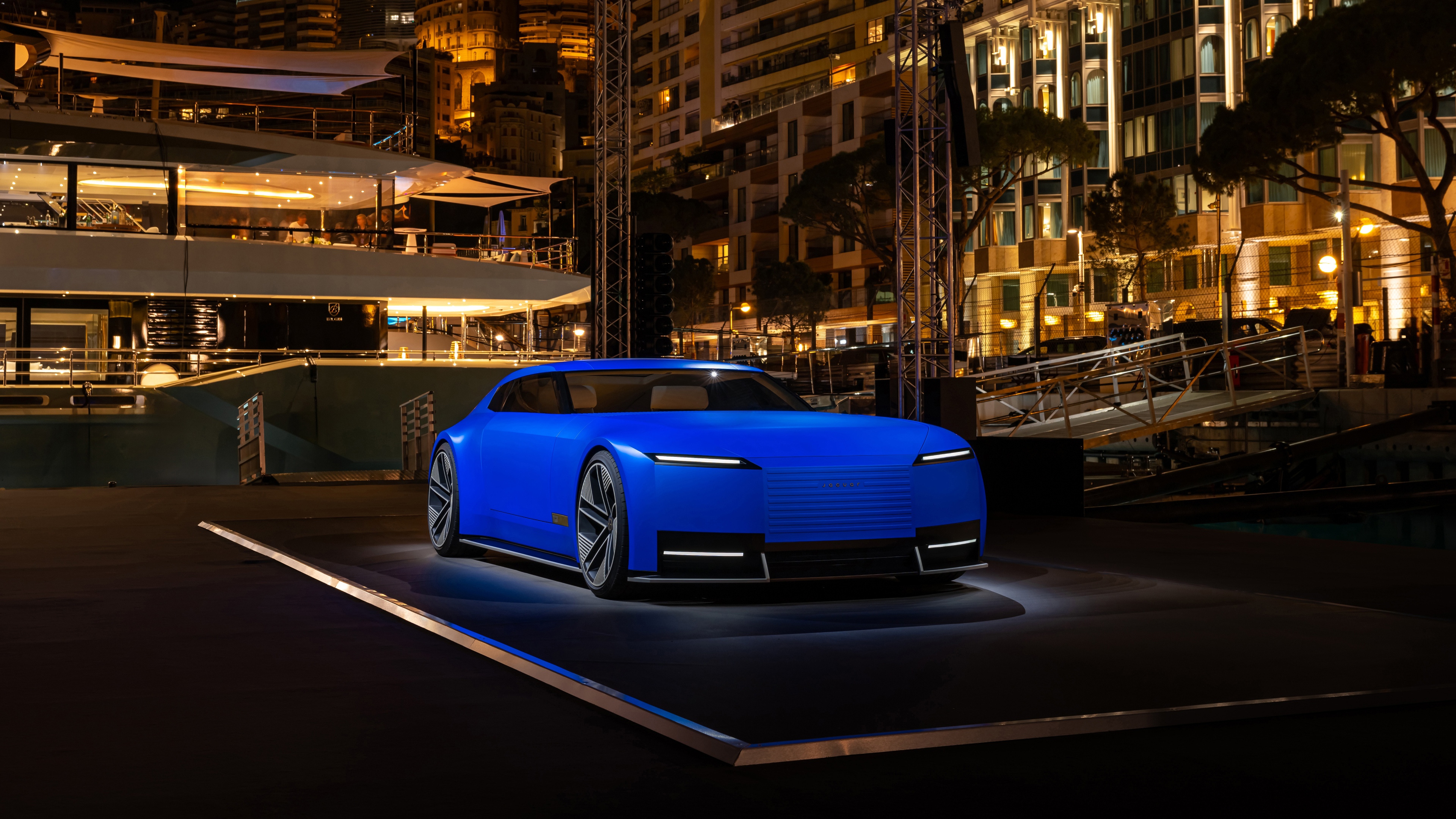 A sleek Jaguar Type 00 concept car in deep French Ultramarine driving through the neon-lit streets of Monaco at night.