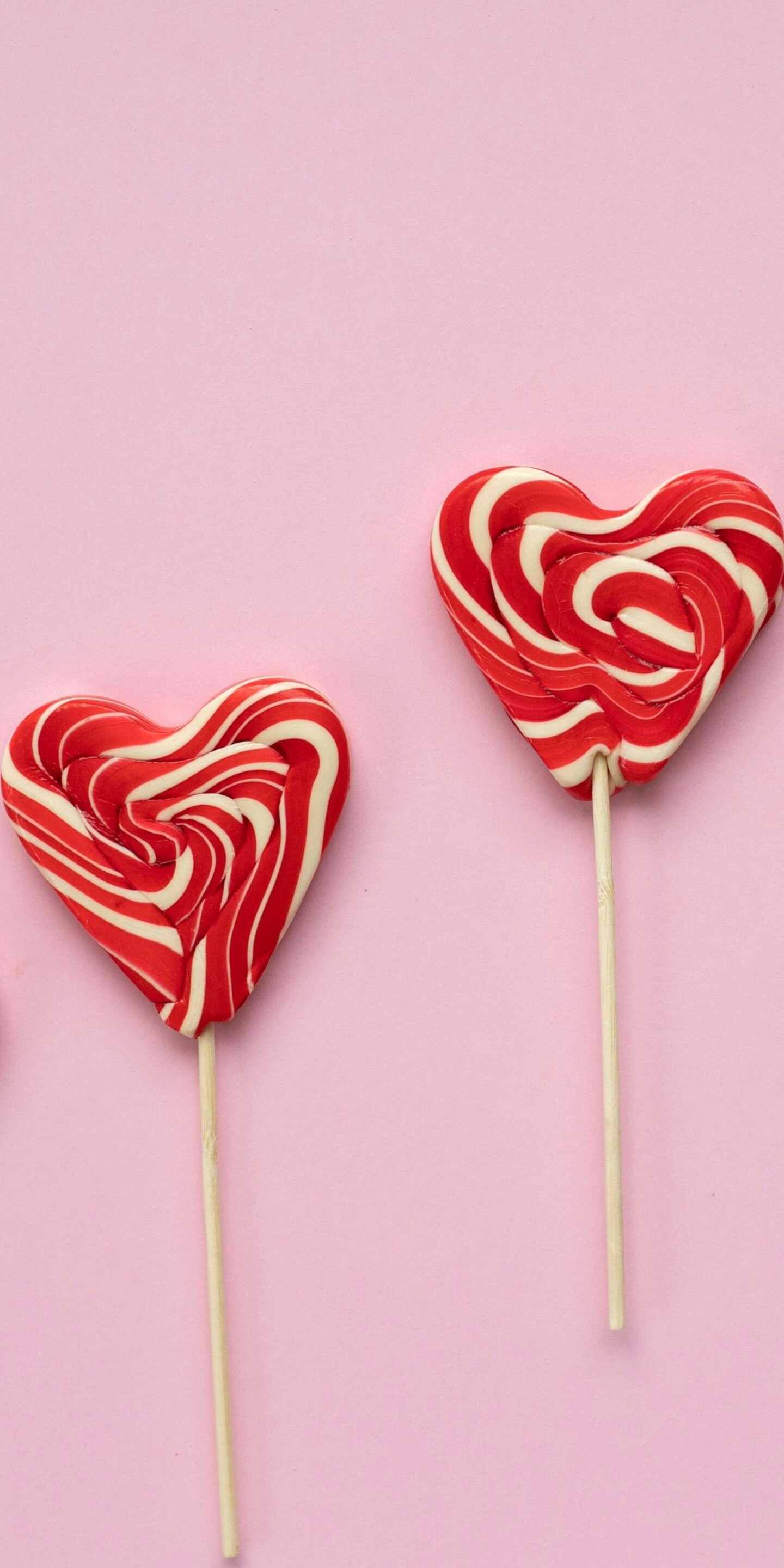 Assorted heart-shaped candies and lollipops in pastel pink and red.