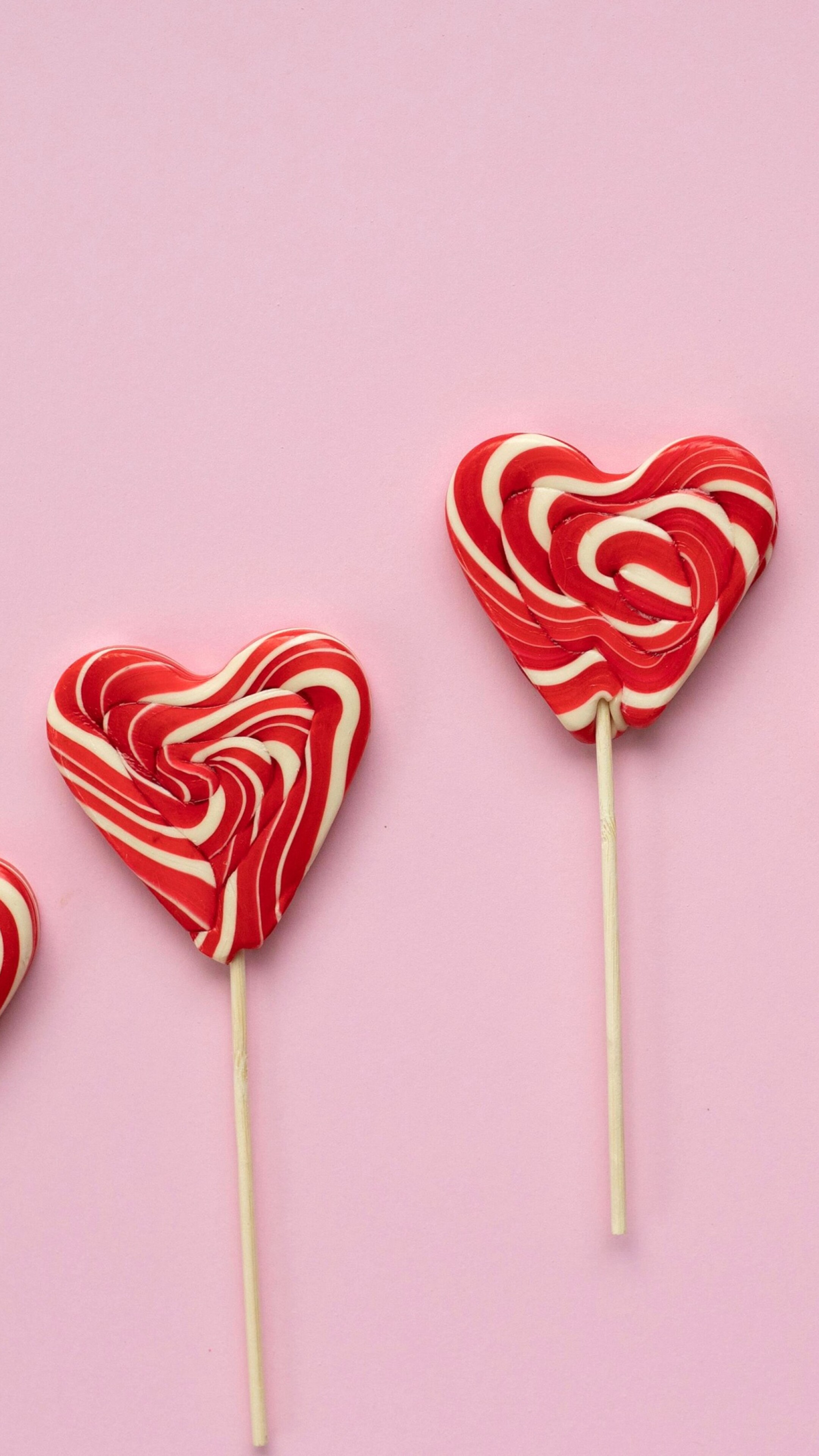 Assorted heart-shaped candies and lollipops in pastel pink and red.