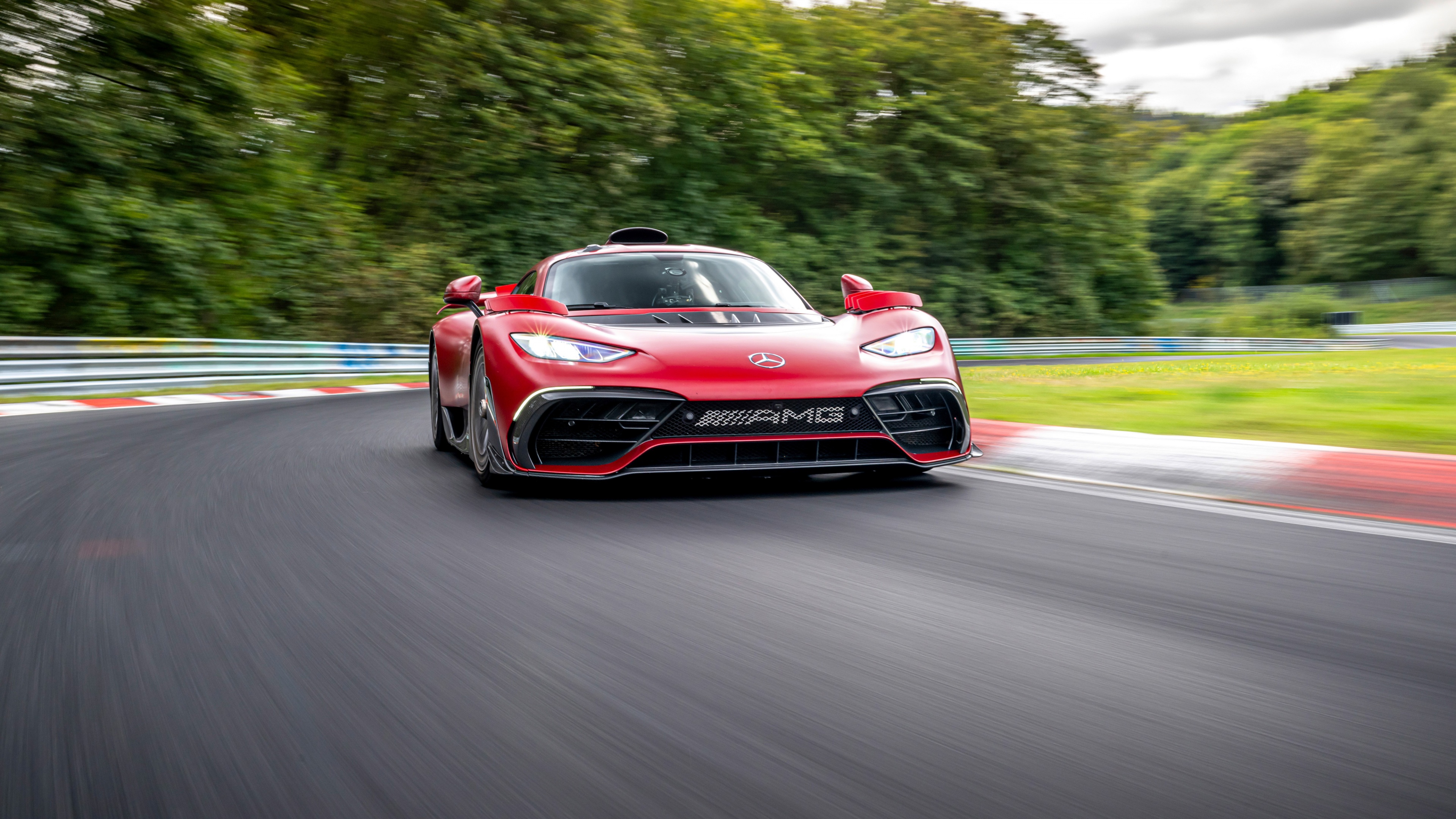 A vibrant red Mercedes-AMG ONE hypercar speeding along a professional race track circuit.