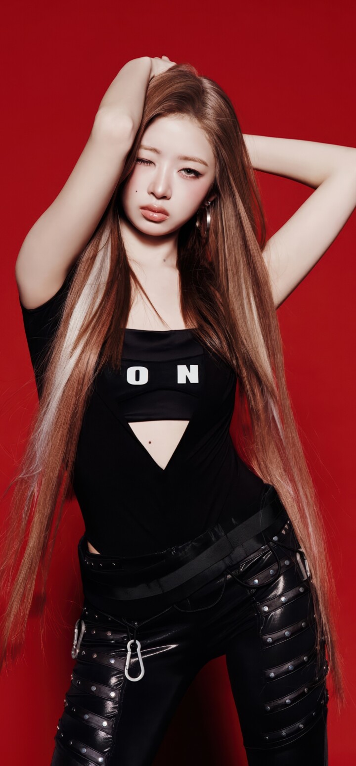 Rei from the K-pop group IVE wearing a black dress against a solid red background