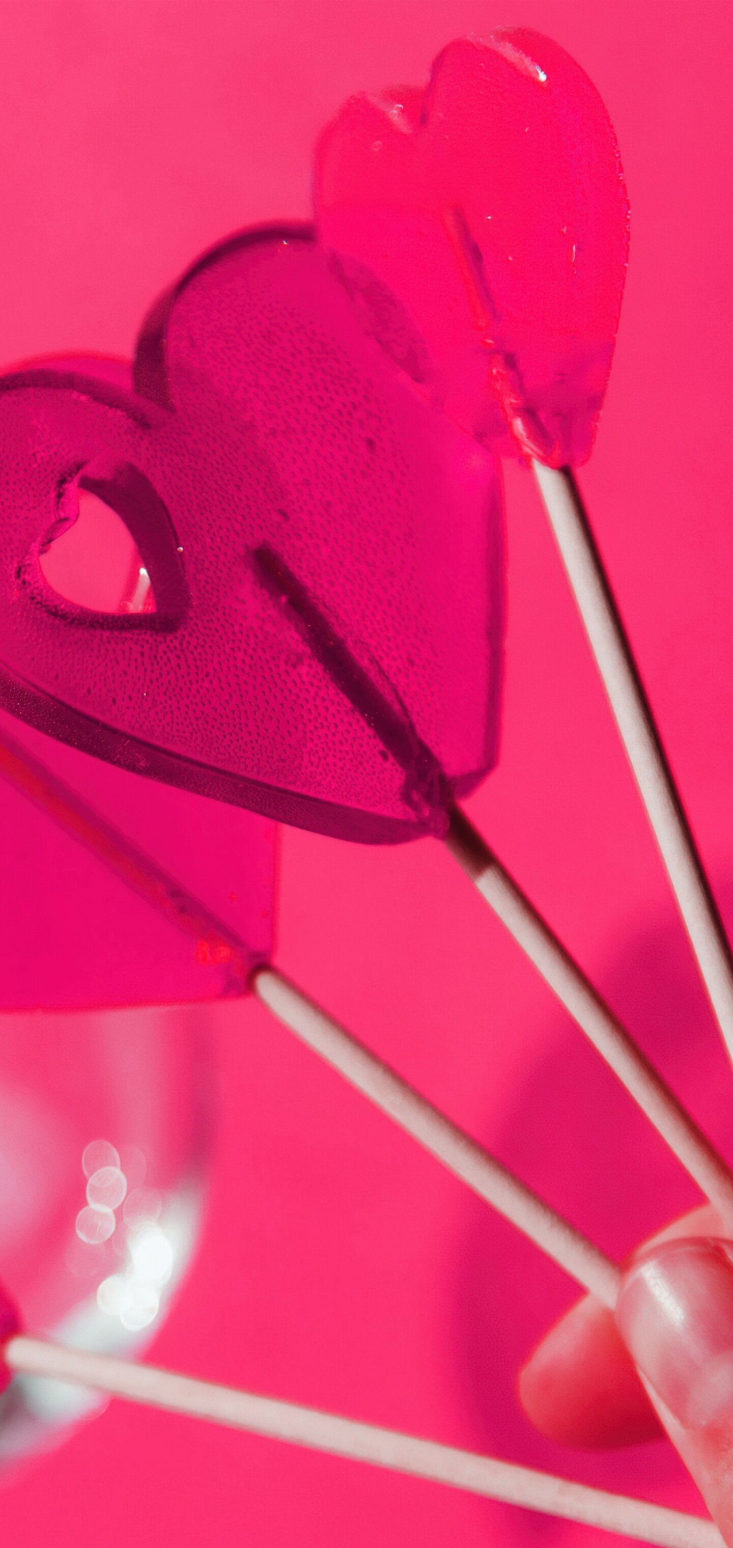 A close-up of a pink lollipop surrounded by various pink hearts on a monochromatic pink background.