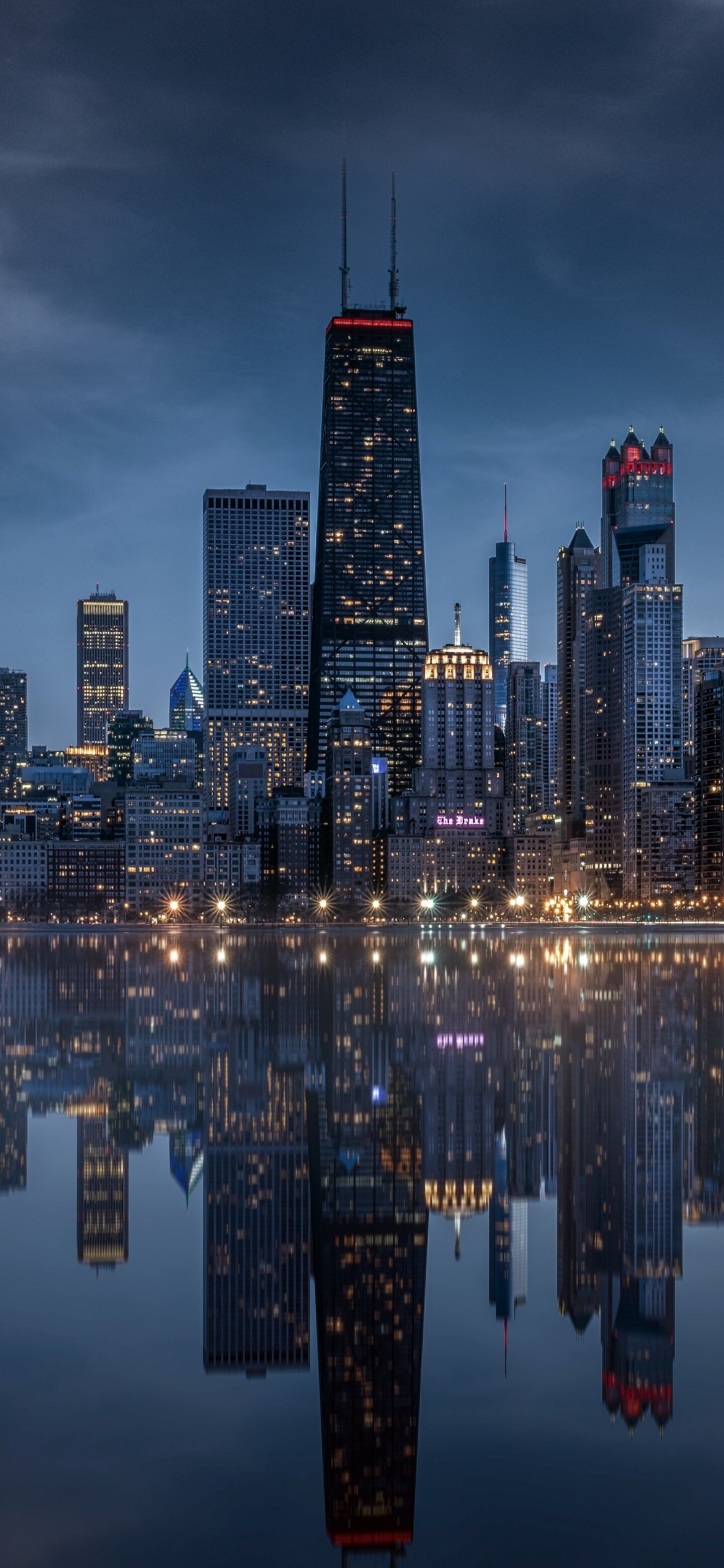Panoramic view of the Chicago city skyline at night with glowing skyscrapers and reflections on the water.