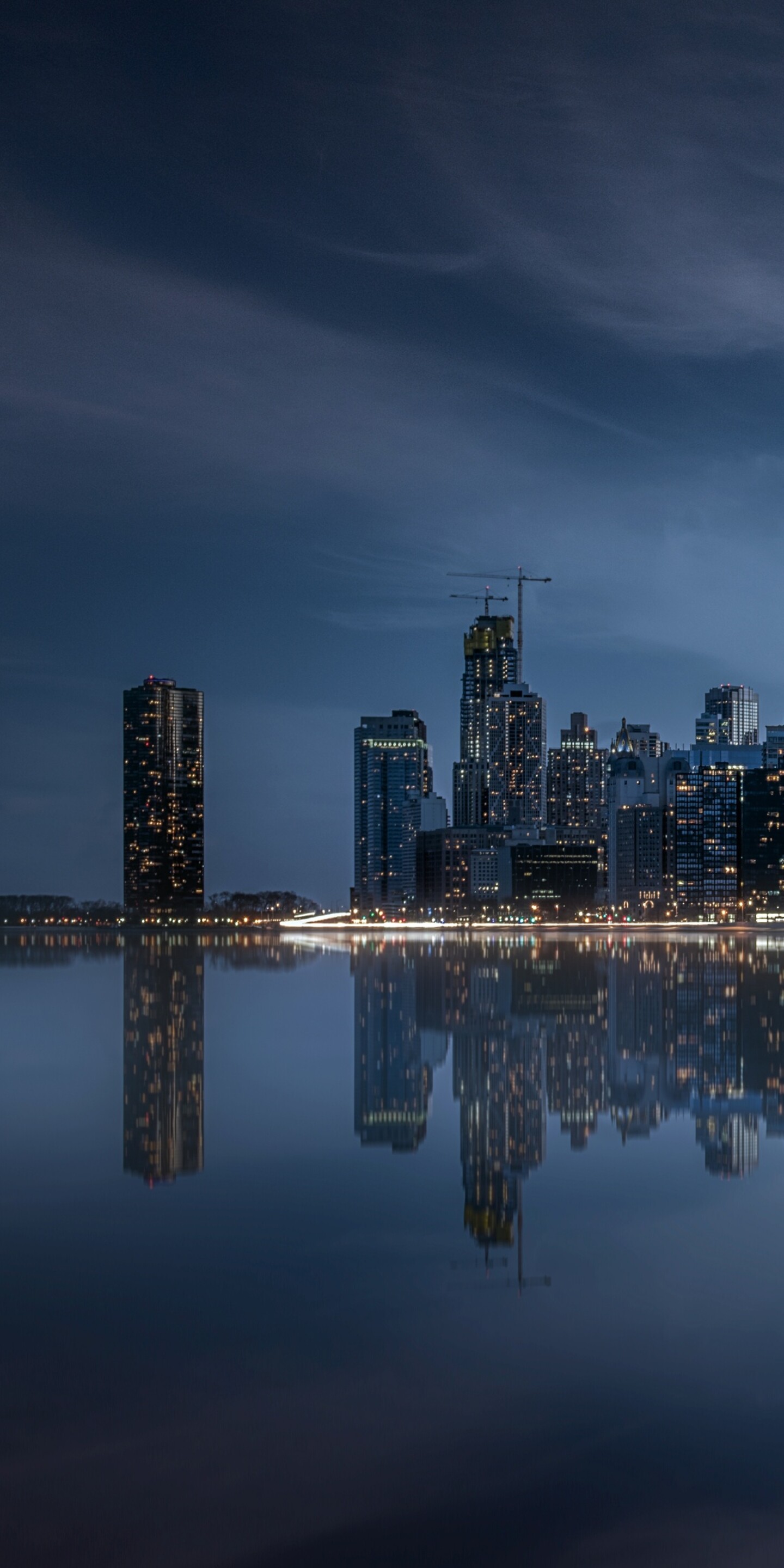 A dramatic night view of the Chicago skyline with illuminated skyscrapers and vibrant city lights reflecting on the water.