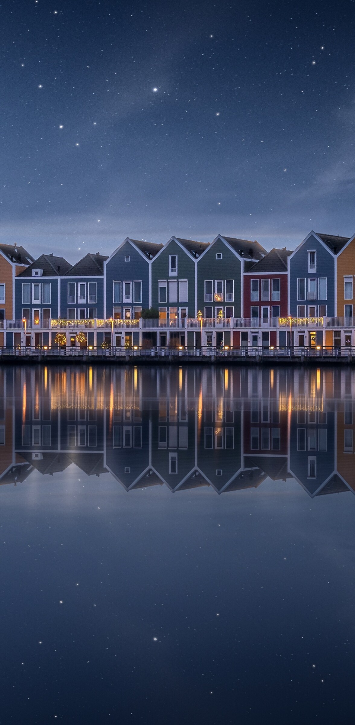 A colorful wooden house by a lake in the Netherlands under a starry evening sky with a rainbow reflection.