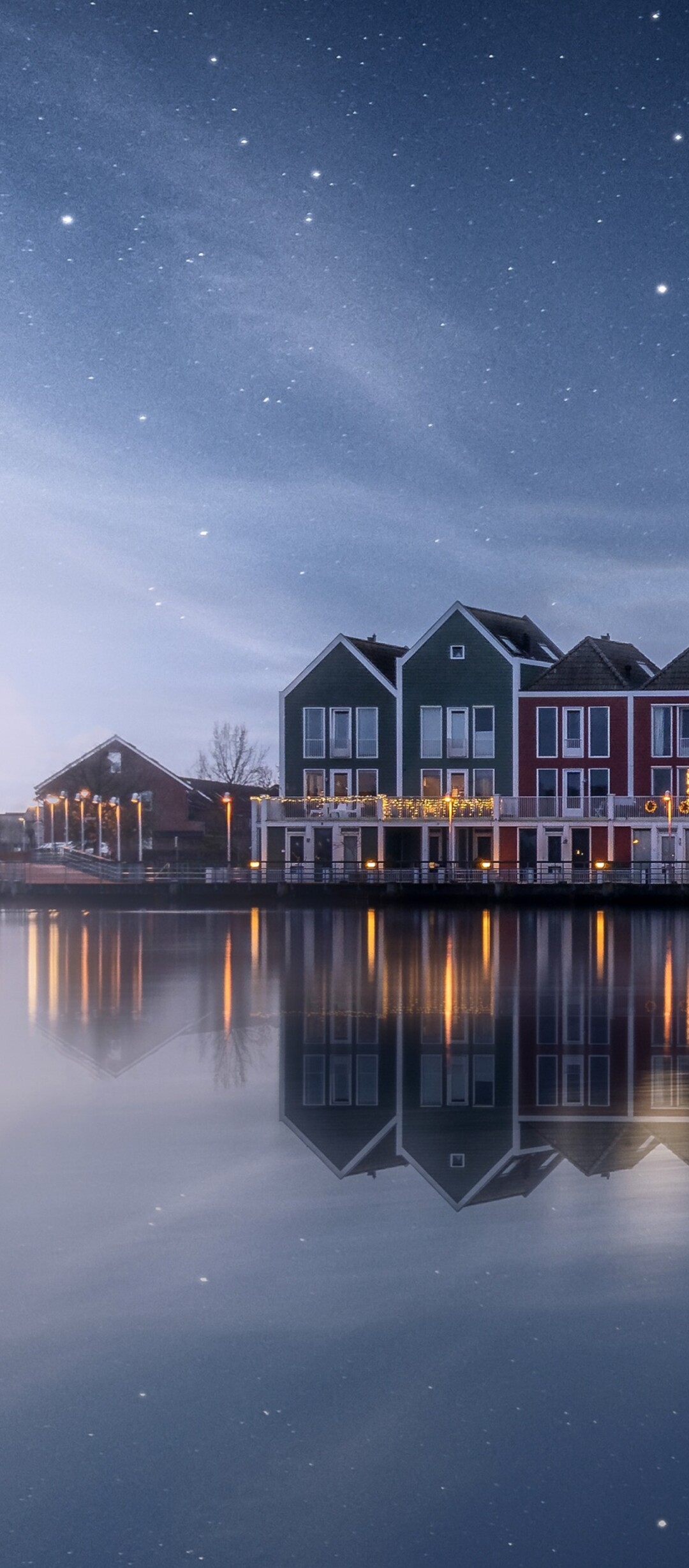 A scenic view of a colorful wooden house by a lakeside in the Netherlands under a starry evening sky with a rainbow and water reflections.