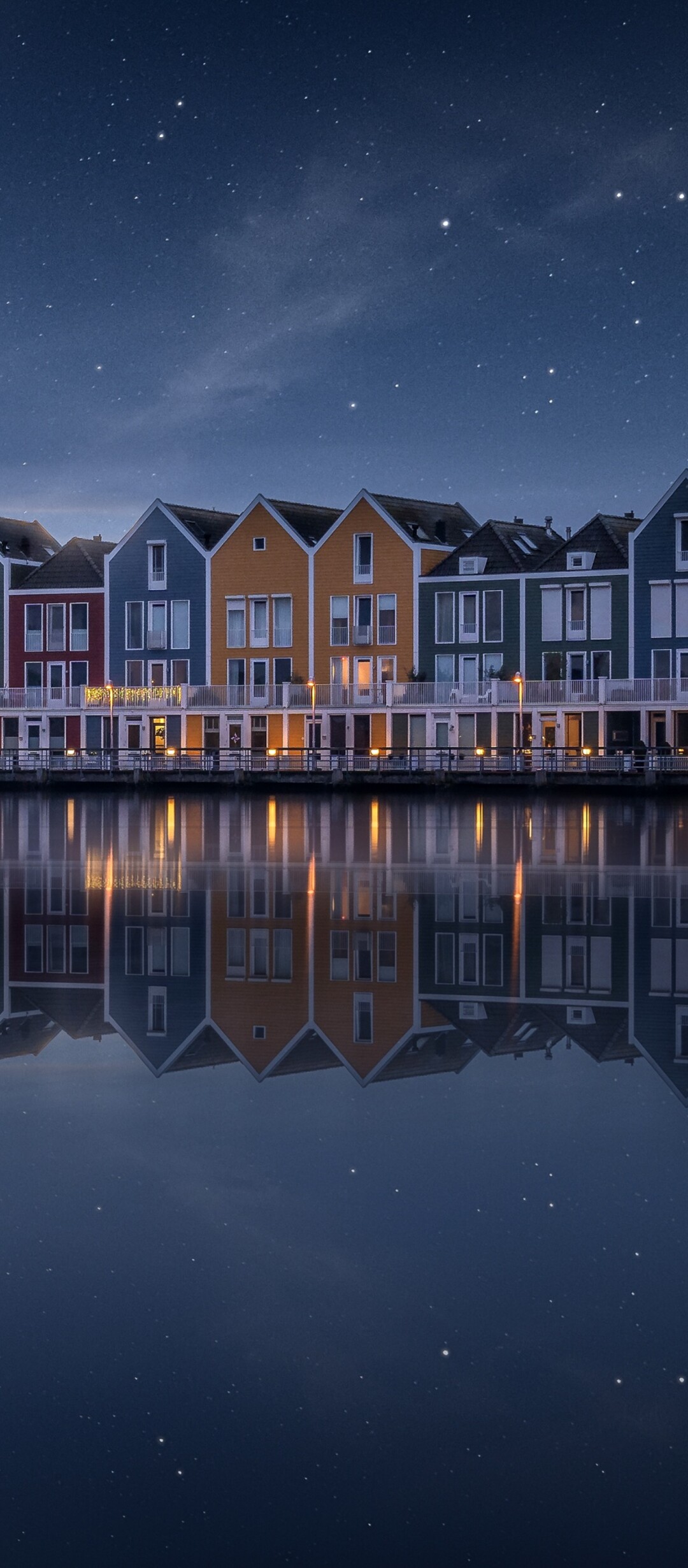 A colorful wooden house by a lake in the Netherlands under a starry evening sky with a rainbow and reflections in the water.