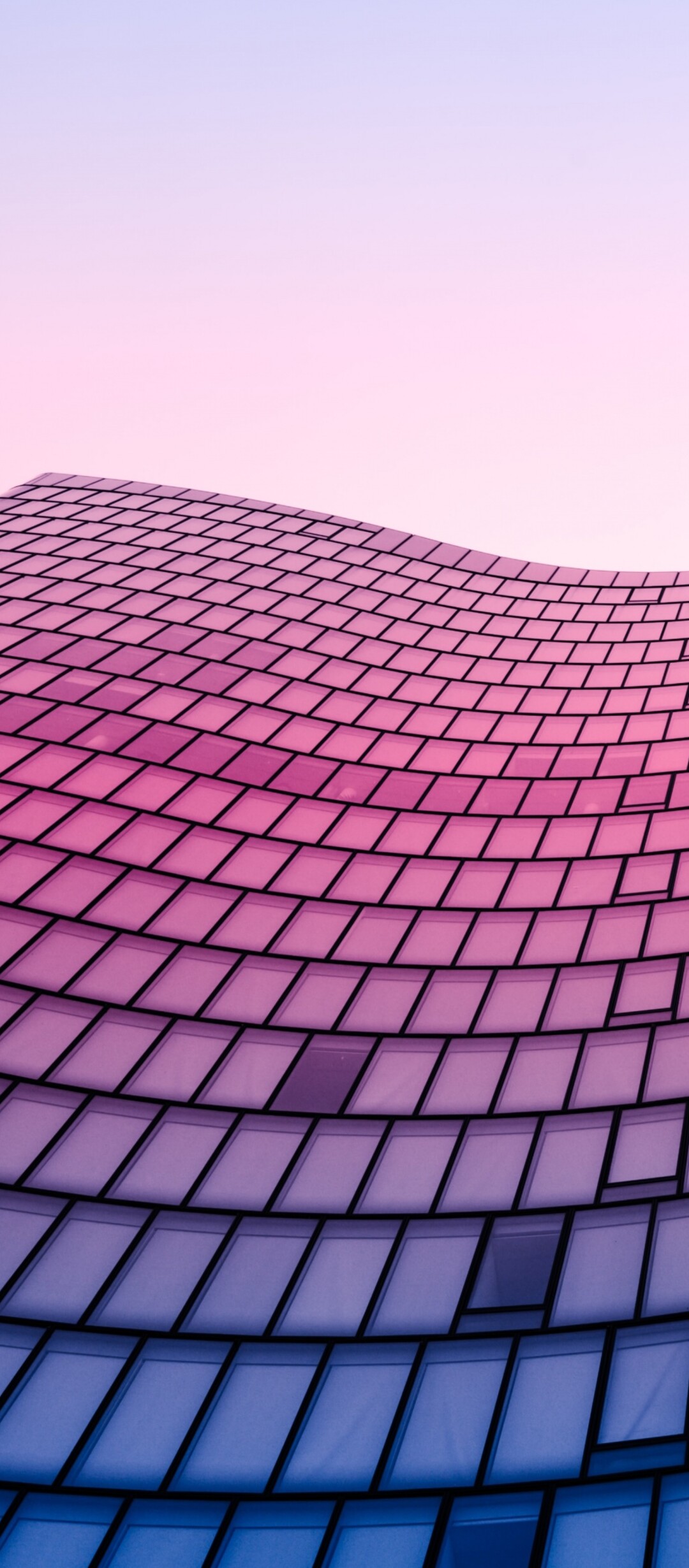Low angle shot looking up at a vibrant glass skyscraper with geometric patterns against a clear sky.