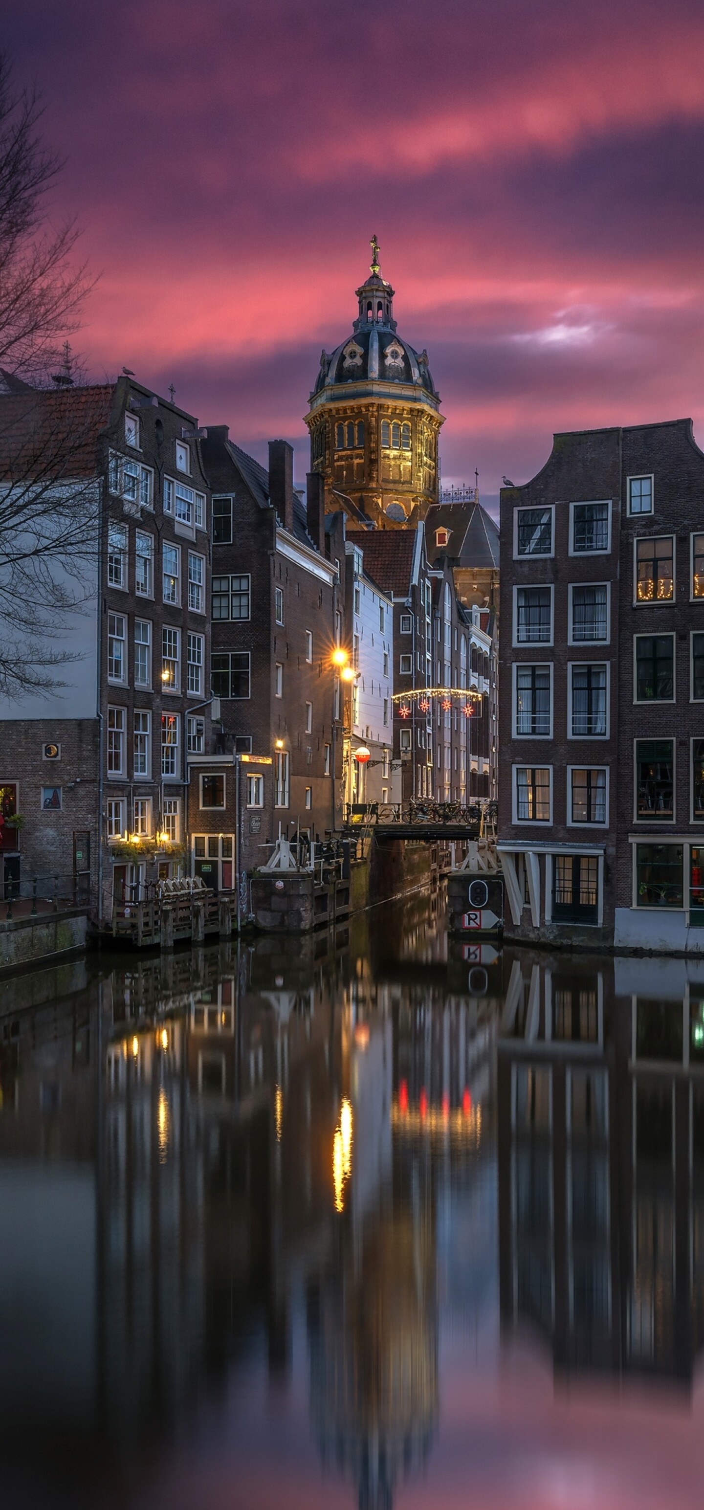 A scenic night view of Amsterdam canals with sunset reflections on the water and historic buildings.