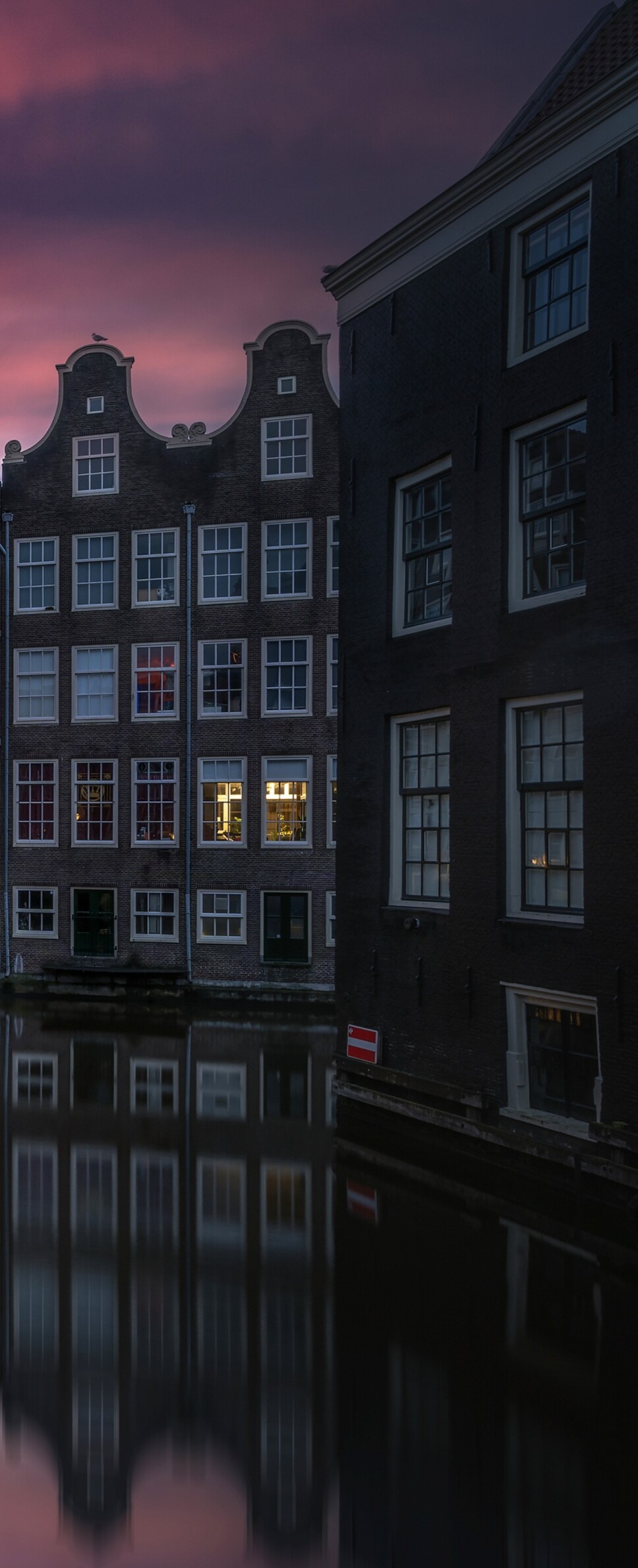 A scenic view of Amsterdam's canals at sunset with illuminated historic buildings and water reflections.