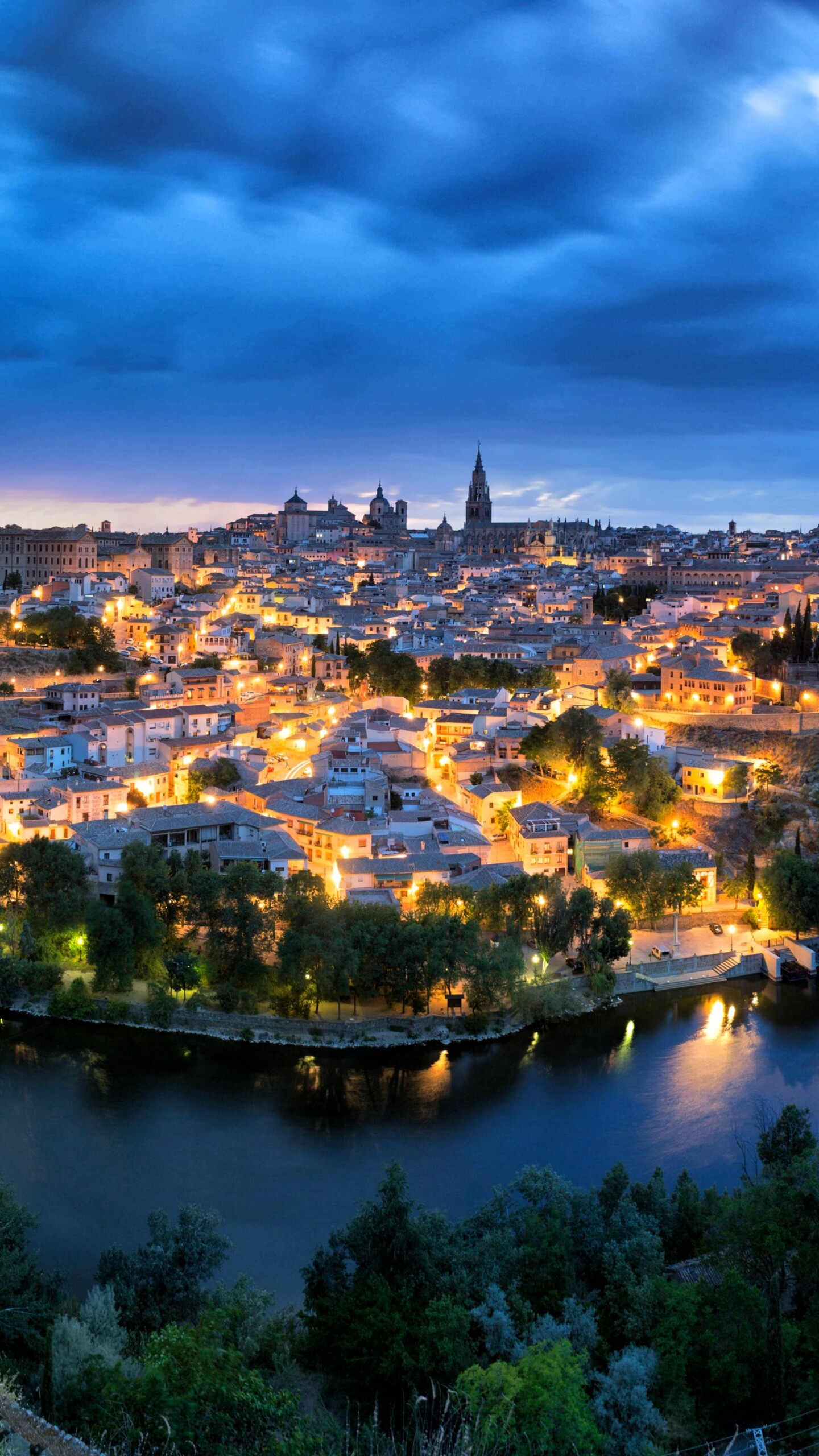 A wide panoramic view of a Spanish cityscape at night, featuring glowing urban lights and a dark night sky.