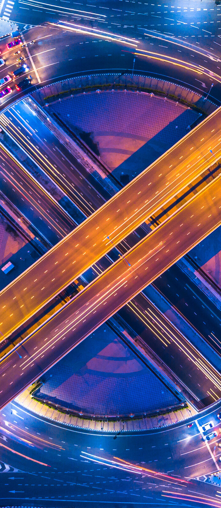 An aerial long exposure shot of a bustling Bangkok intersection at night featuring colorful traffic light trails.