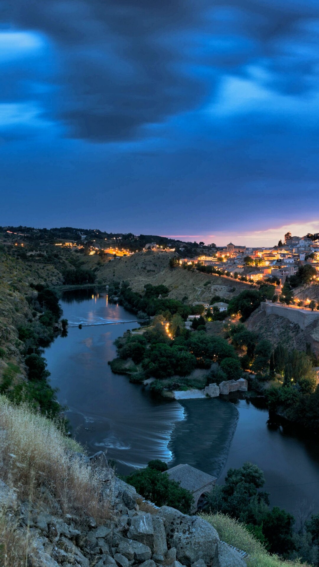 A panoramic night view of a Spanish city skyline featuring glowing city lights and urban architecture.