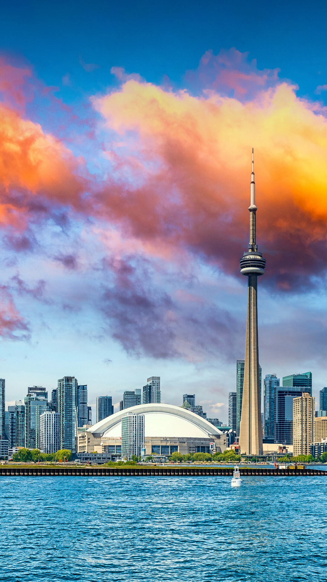 Panoramic view of the Toronto skyline featuring the CN Tower and Lake Ontario under a cloudy sky.