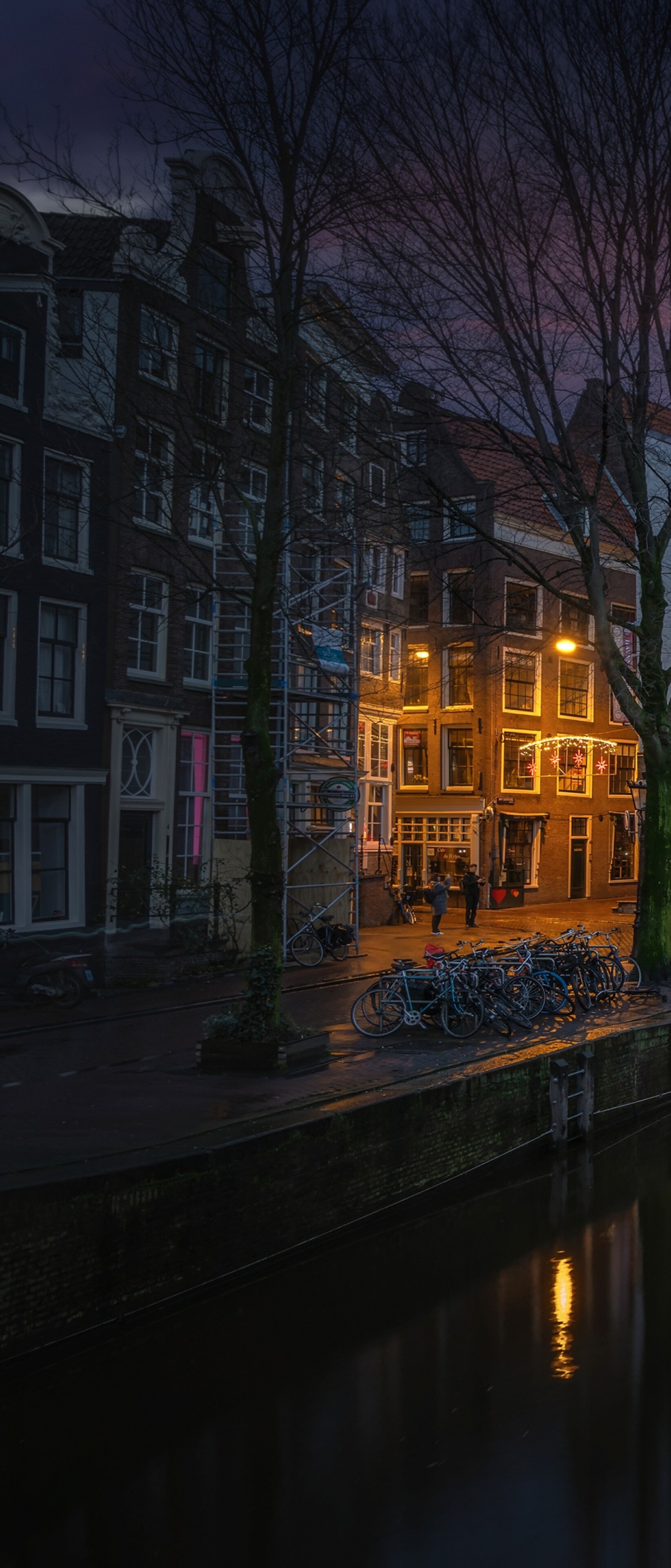 A scenic nighttime view of Amsterdam's canals with sunset reflections on the water and illuminated historic buildings.