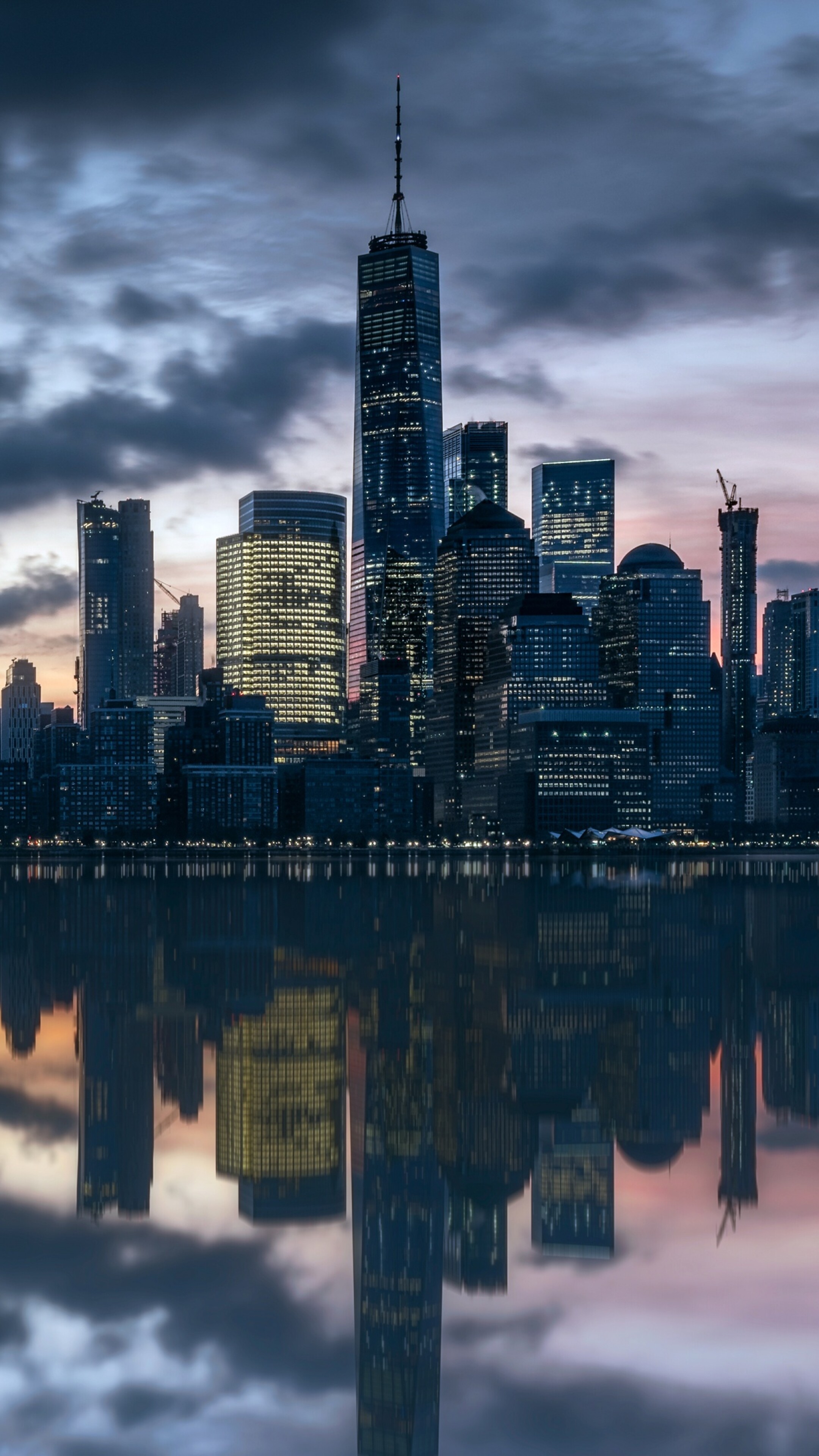 Manhattan skyline at dusk with skyscrapers reflecting in the Hudson River.