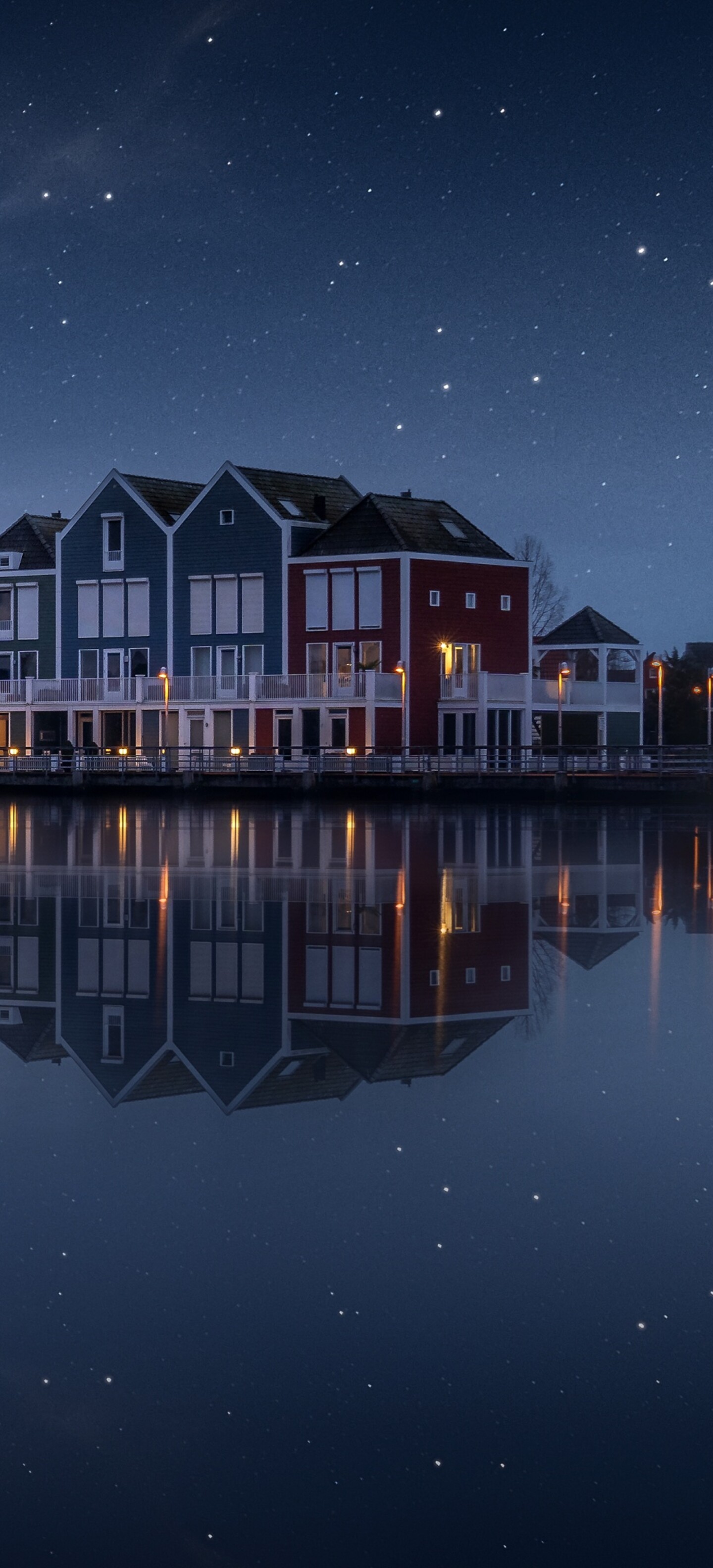 A colorful wooden house by a lake in the Netherlands under a starry evening sky with a rainbow and reflections.