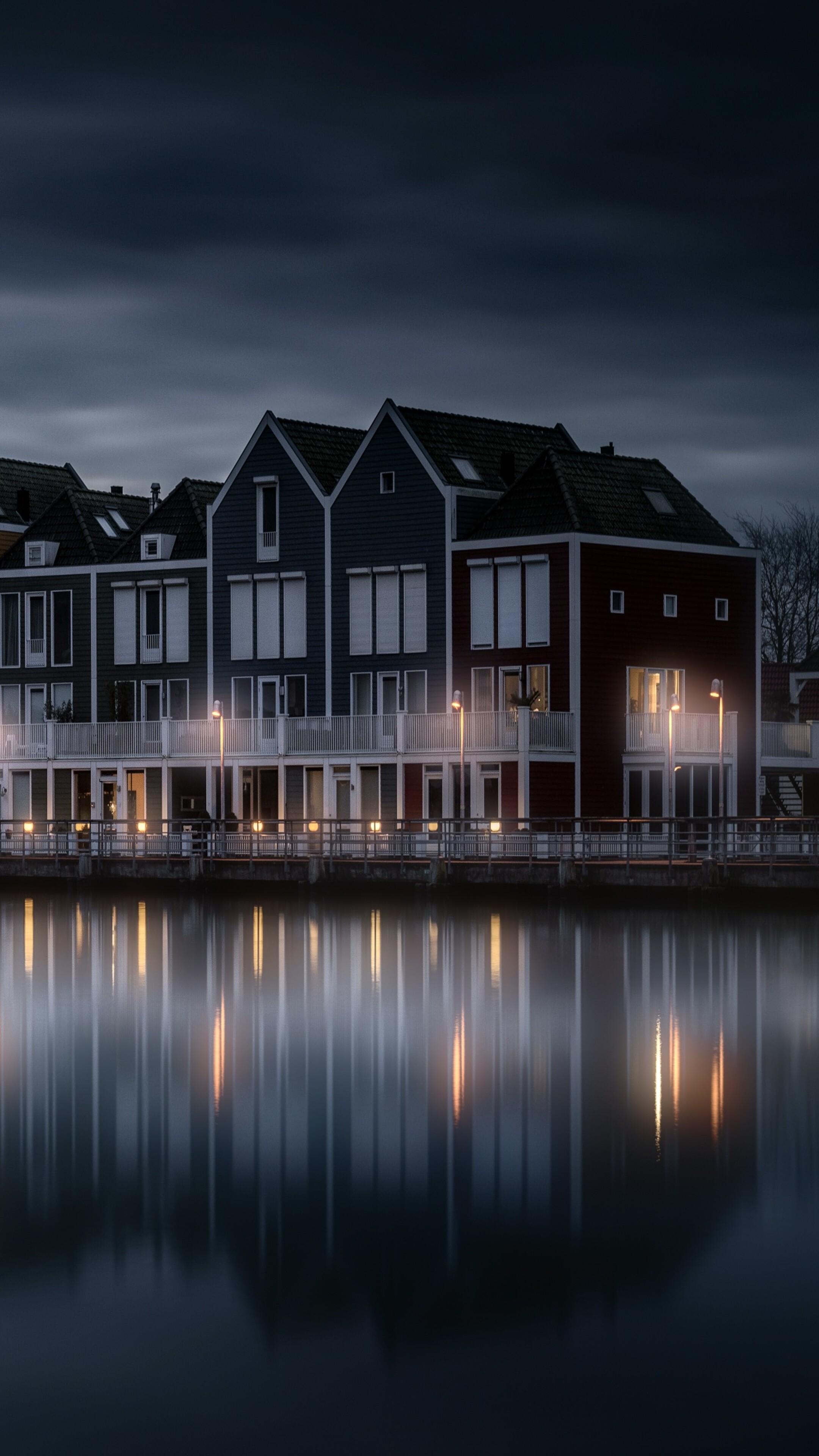 A scenic view of a wooden house by a lake in the Netherlands during a colorful evening with dark clouds reflecting in the water.