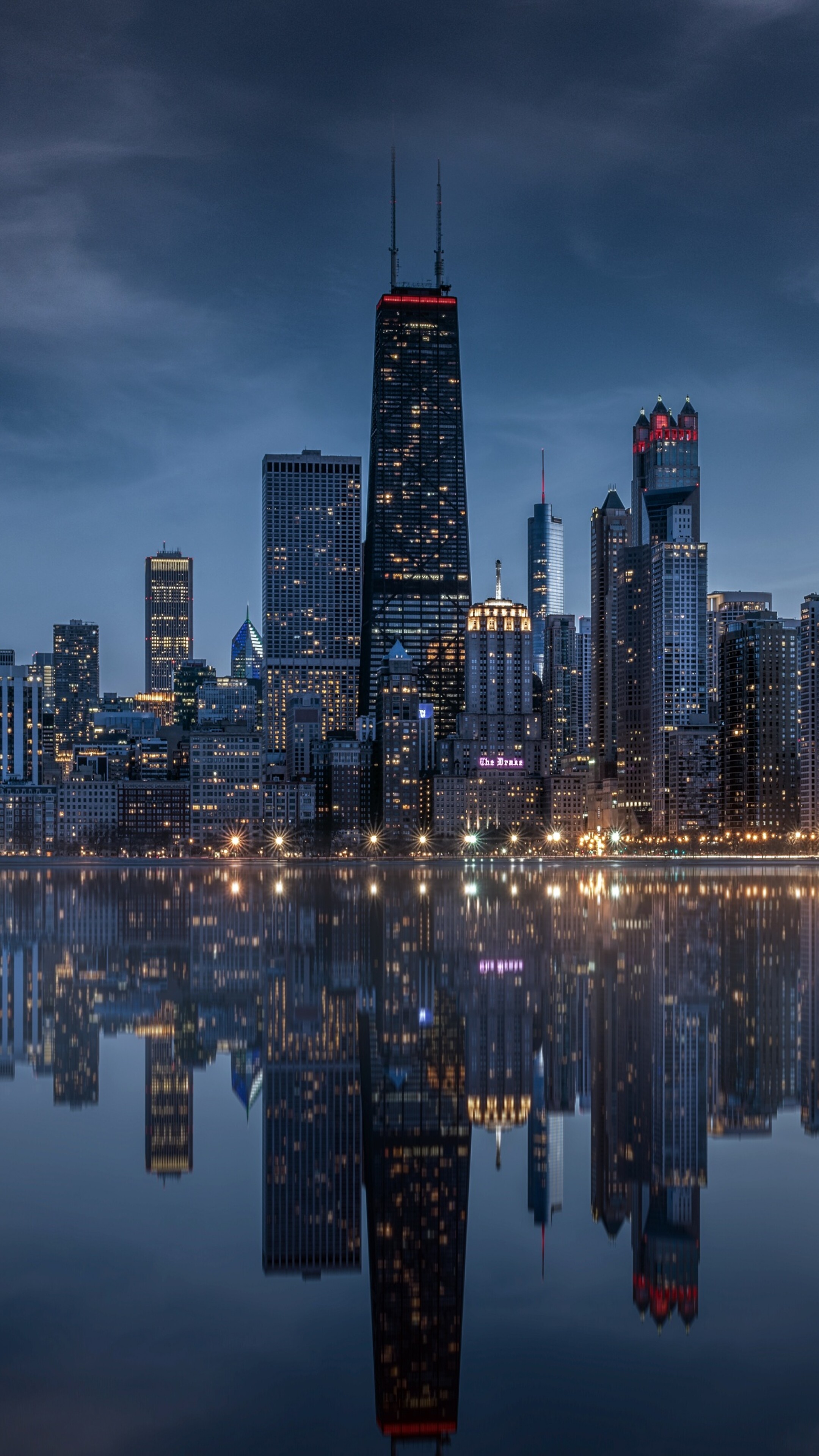 Panoramic view of the Chicago city skyline at night with glowing skyscrapers and reflections on the water.