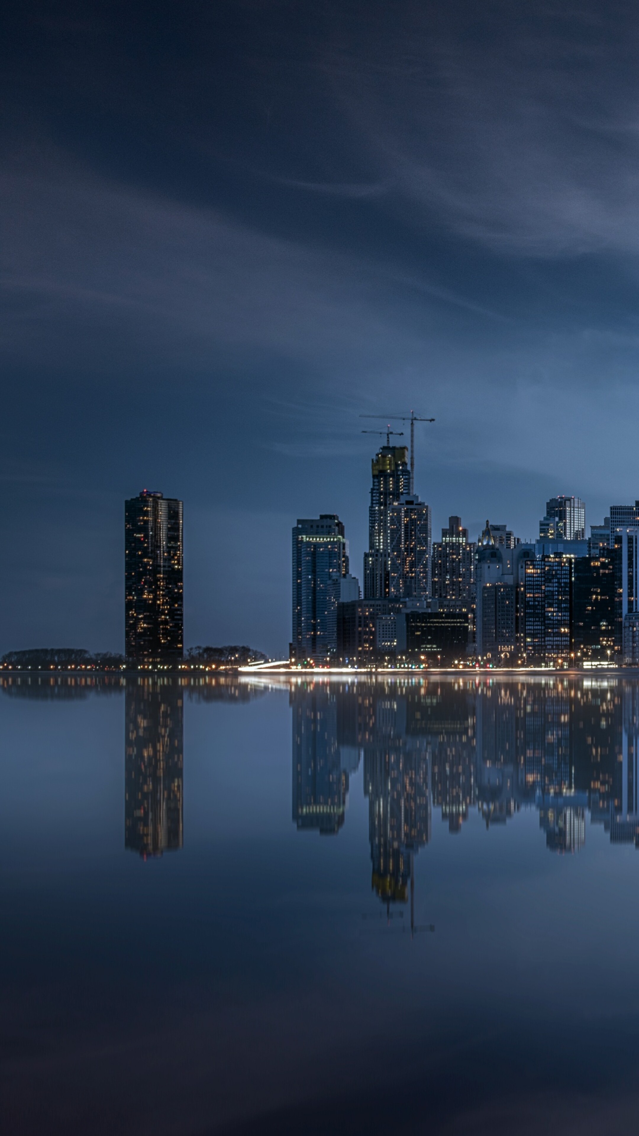 A dramatic night view of the Chicago skyline with illuminated skyscrapers and vibrant city lights reflecting on the water.