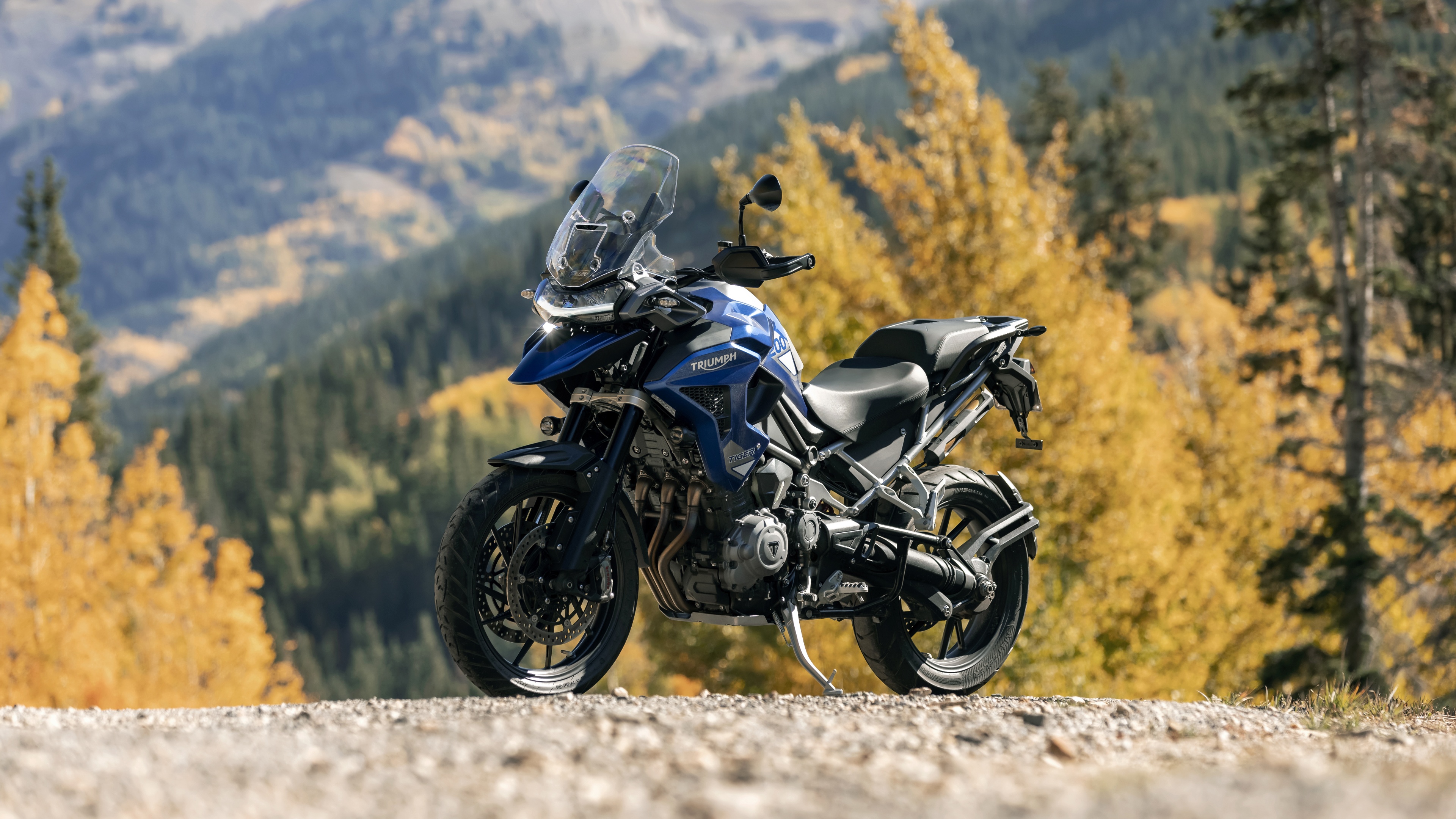 A detailed shot of heavy-duty adventure motorcycles parked on a dusty trail in a scenic mountain landscape.