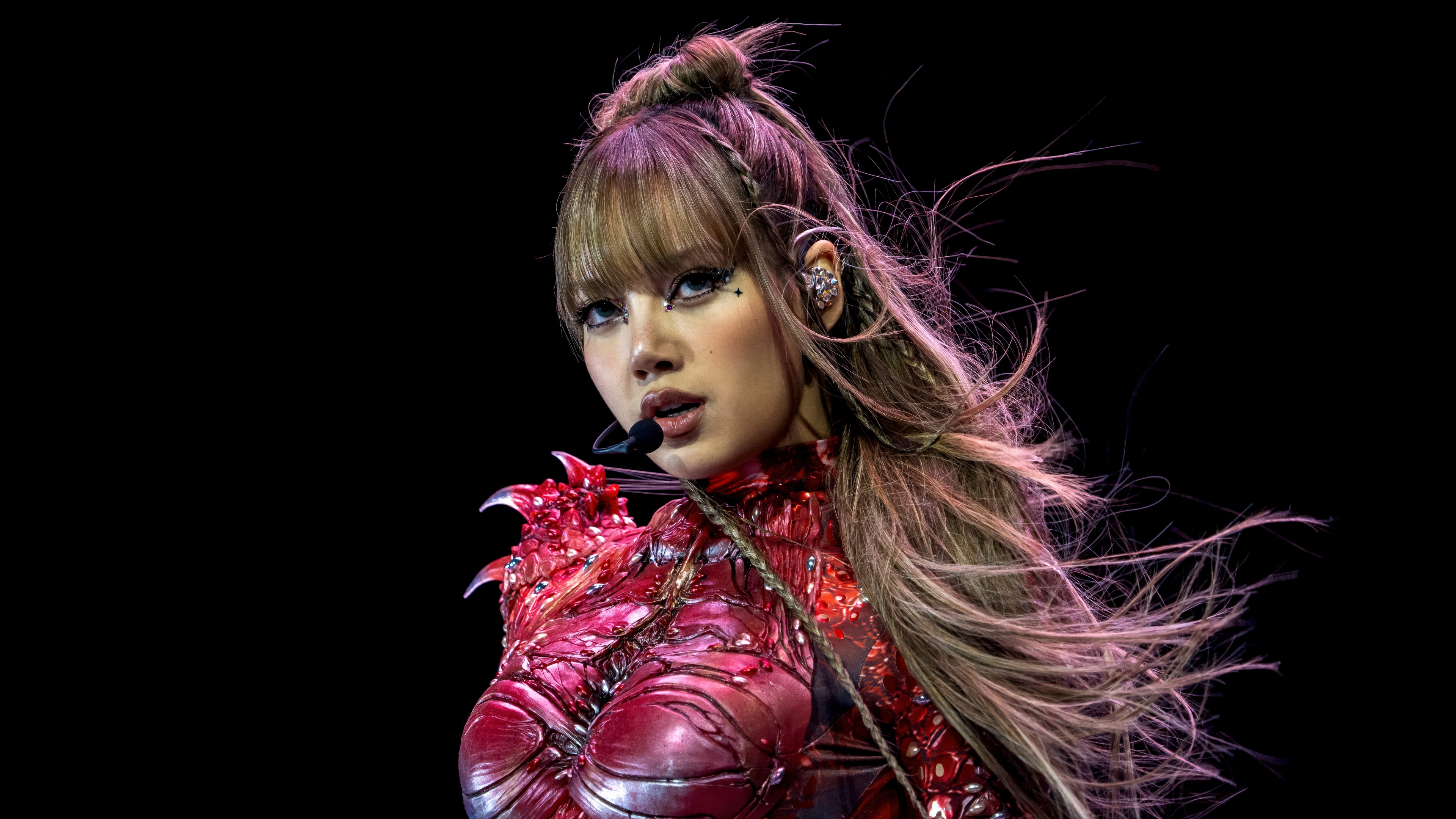 Lisa of BLACKPINK performing on stage during a live concert against a dark black background.