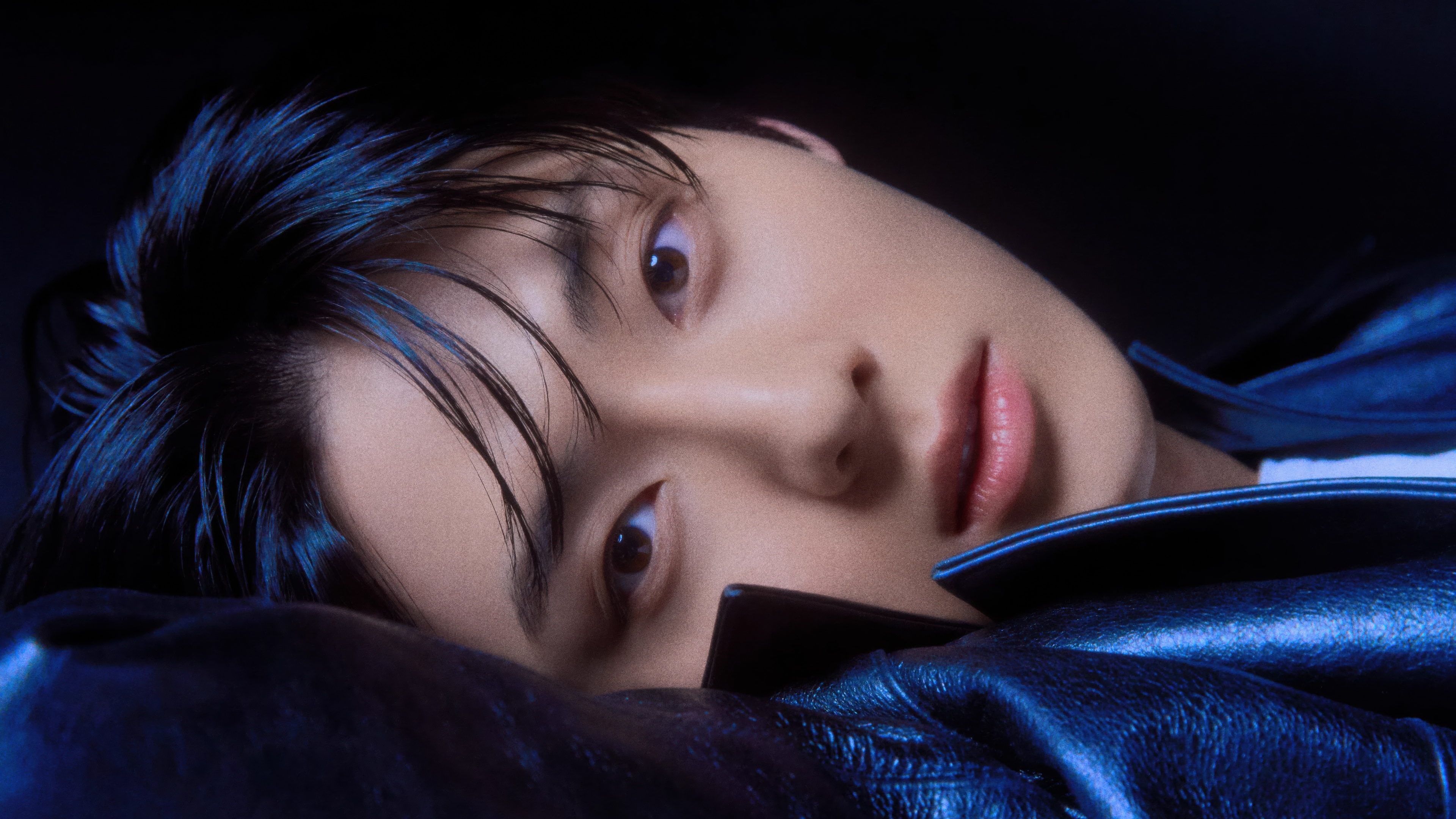 A high-quality close-up portrait of a South Korean singer with dramatic lighting against a dark background.