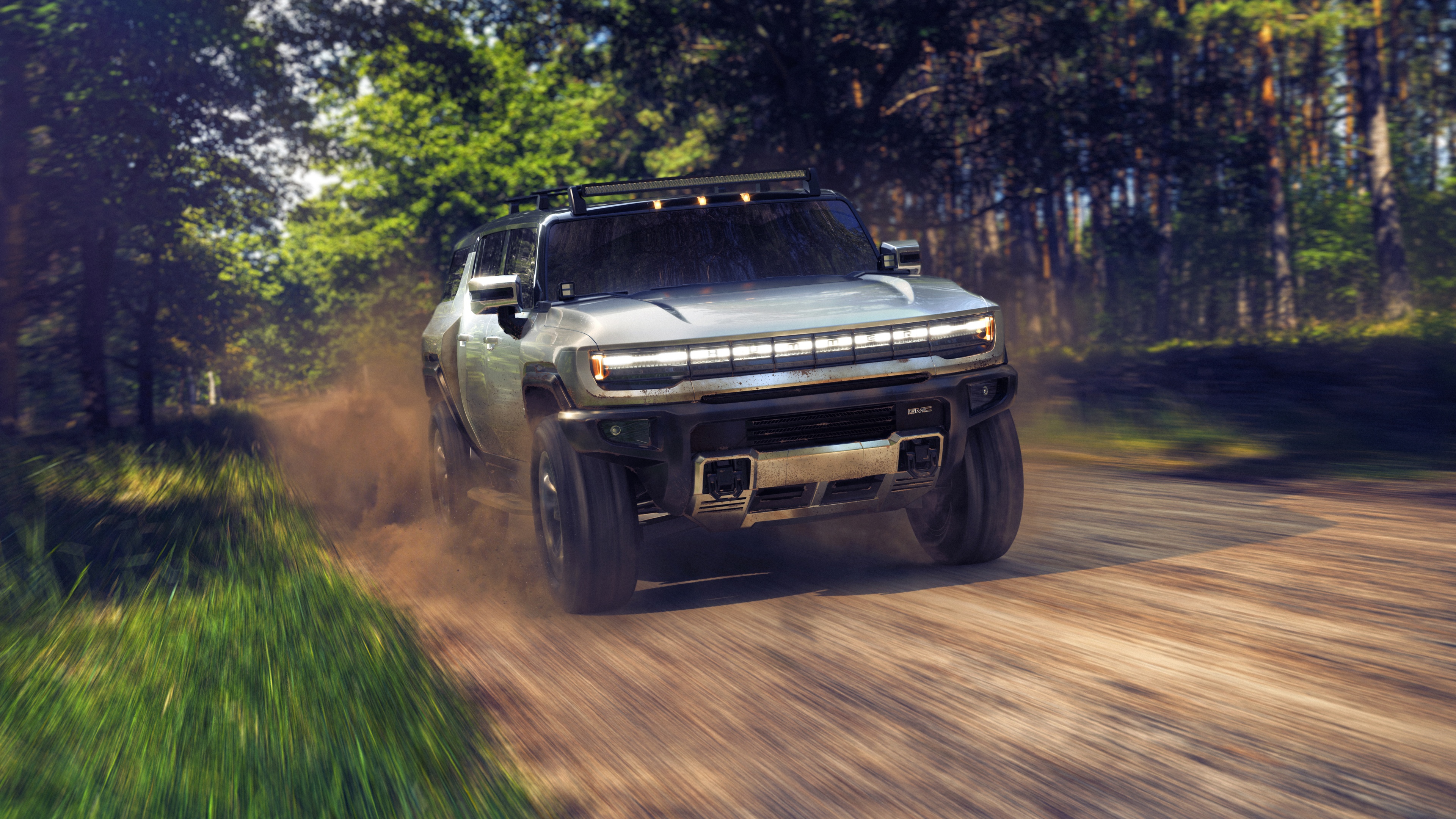 A 2024 GMC Hummer EV electric pickup truck driving on a rugged dirt road.