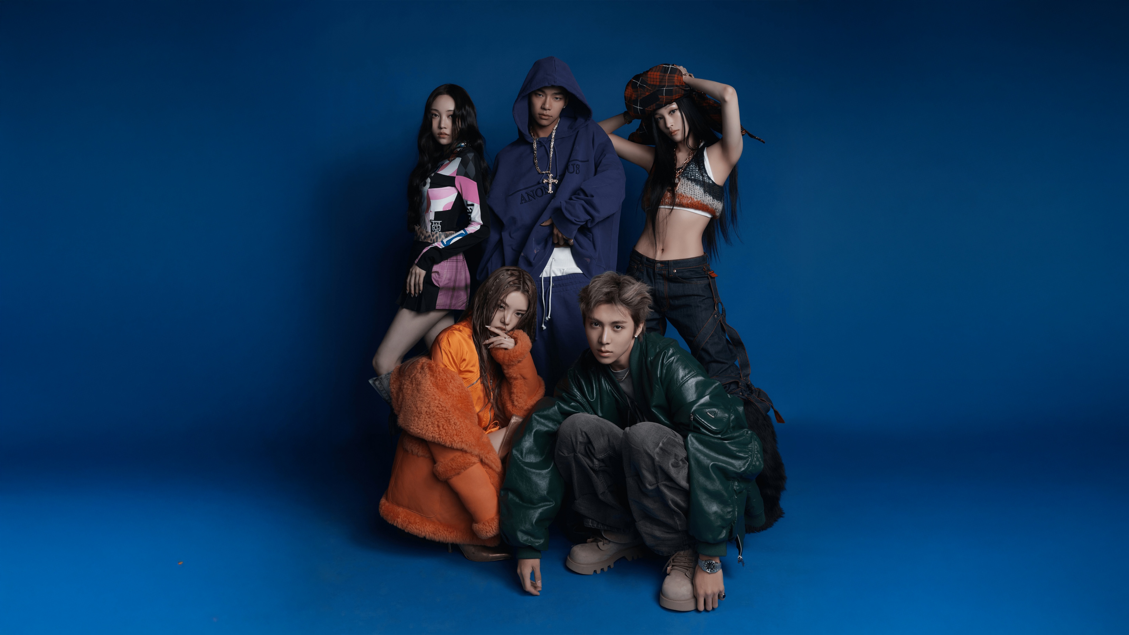The K-Pop group members Youngseo, Annie, Bailey, Tarzzan, and Woochan posing together against a vibrant blue background.