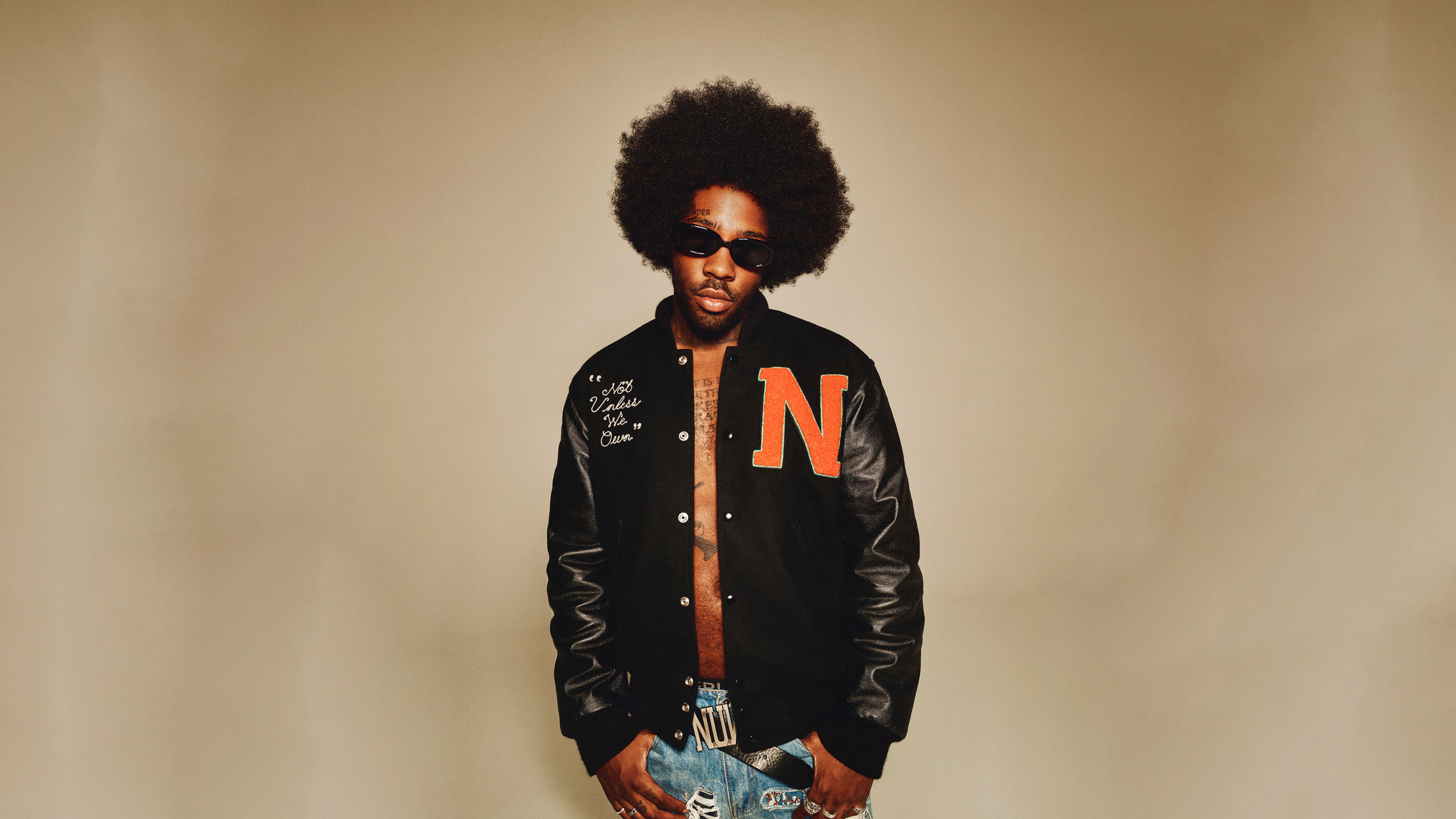 A professional studio portrait of American singer Brent Faiyaz, styled for a Vogue magazine feature against a solid brown background.