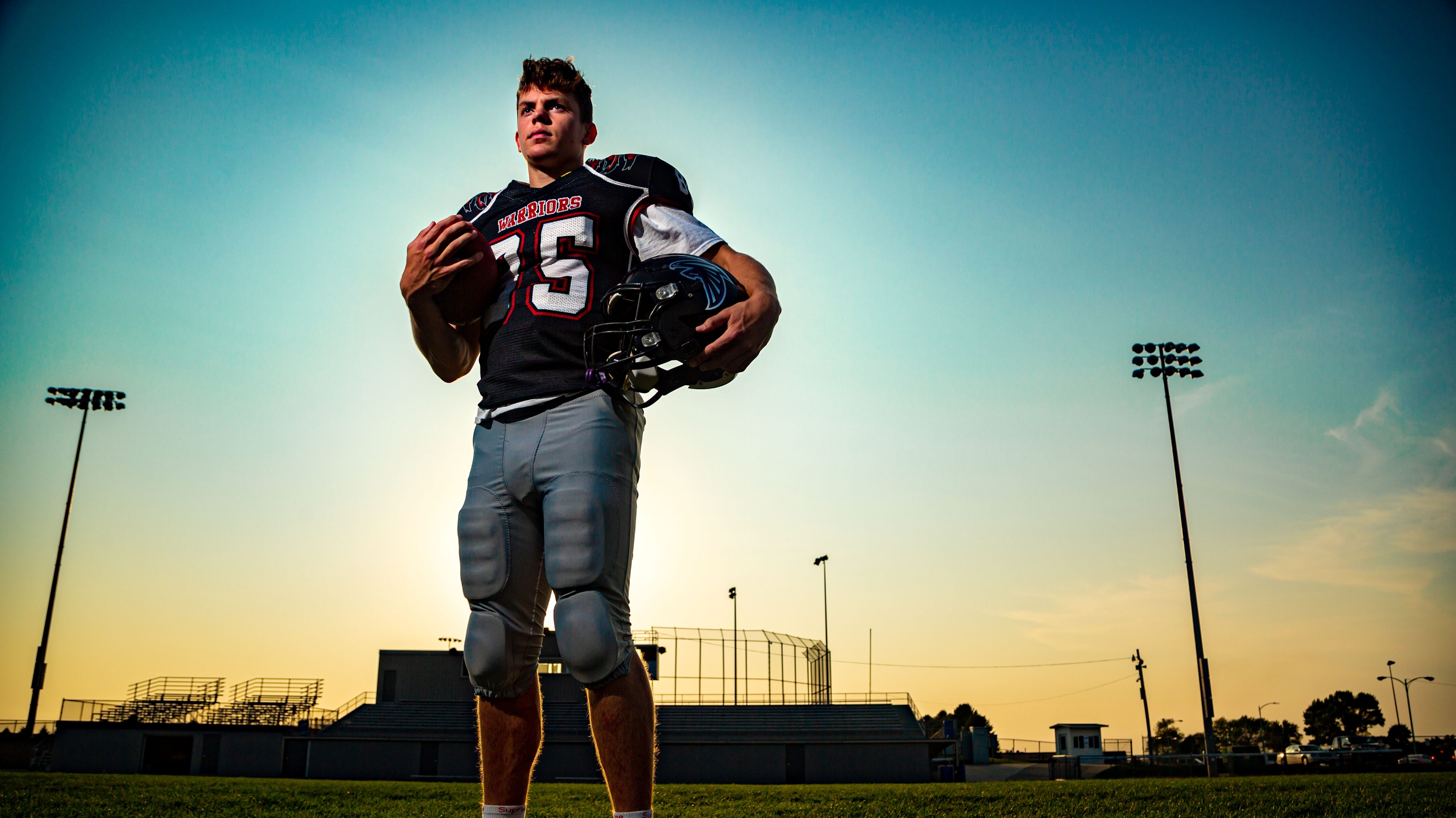 American football player Cooper DeJean posing in a stadium under a vibrant sunset sky.
