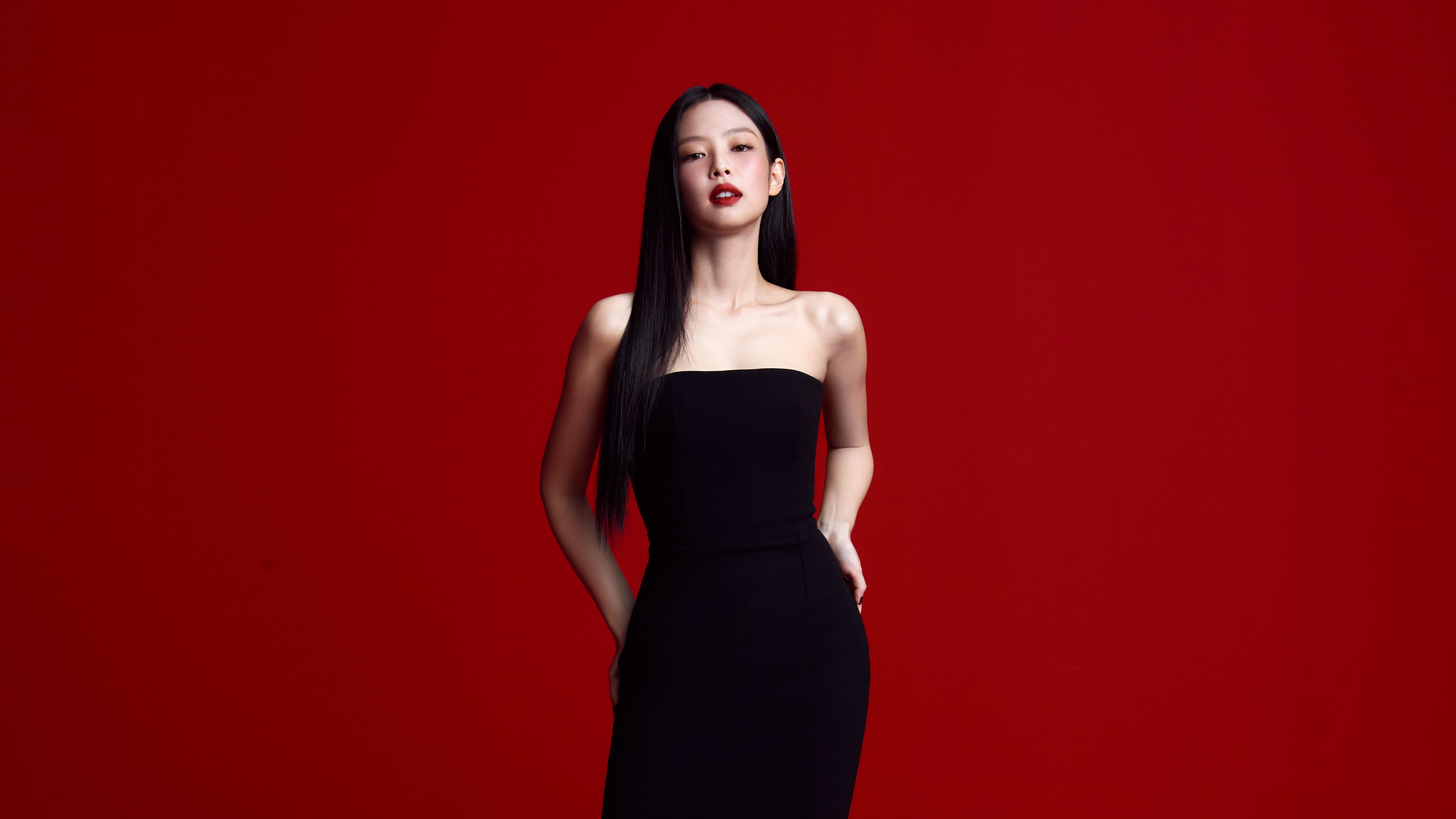 Jennie Kim of BLACKPINK wearing a classy black dress against a bold red background