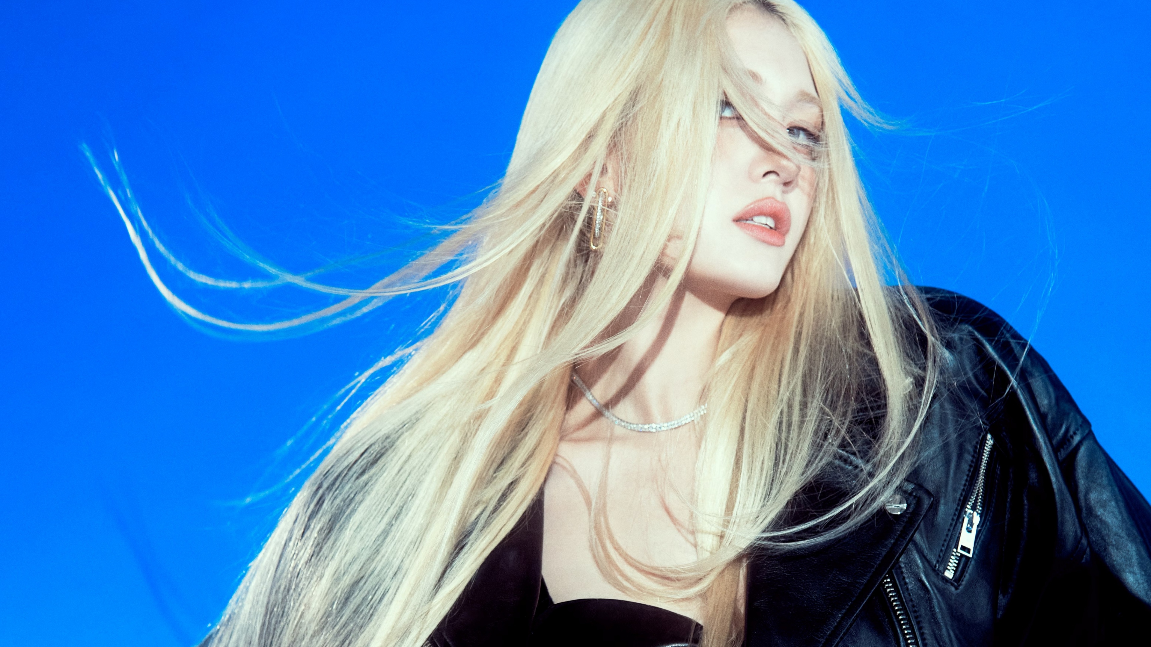 A portrait of K-pop artist Jeon Somi wearing a black jacket against a blue background