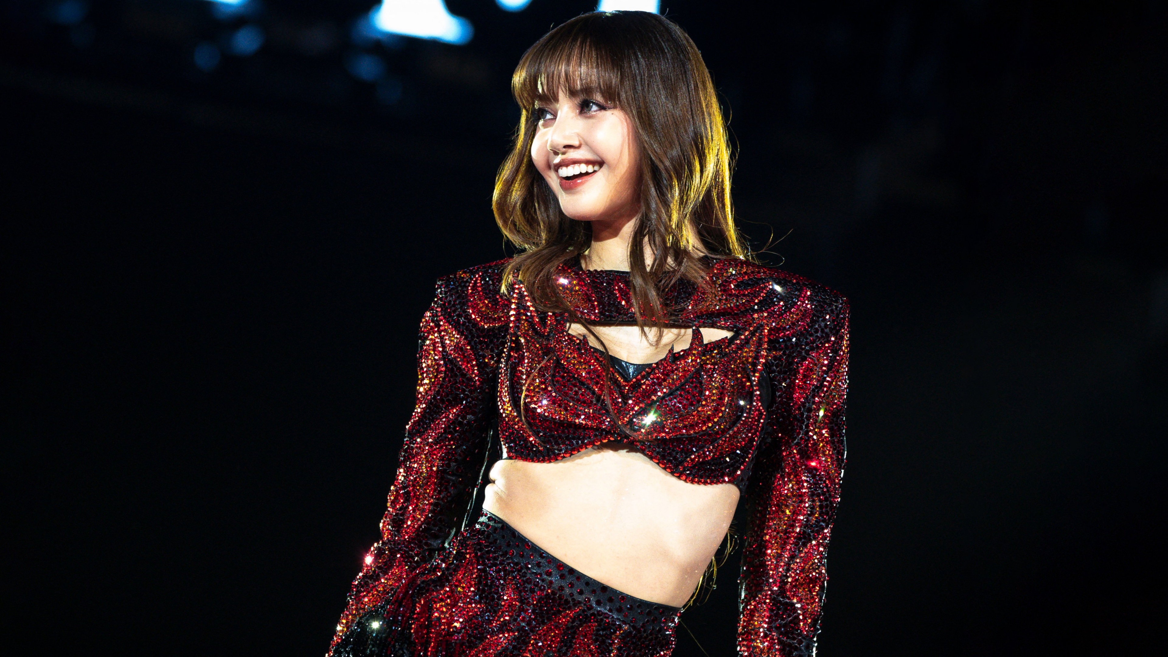K-pop idol Lisa from BLACKPINK performing energetically on stage during a live concert with bright, colorful stage lights.