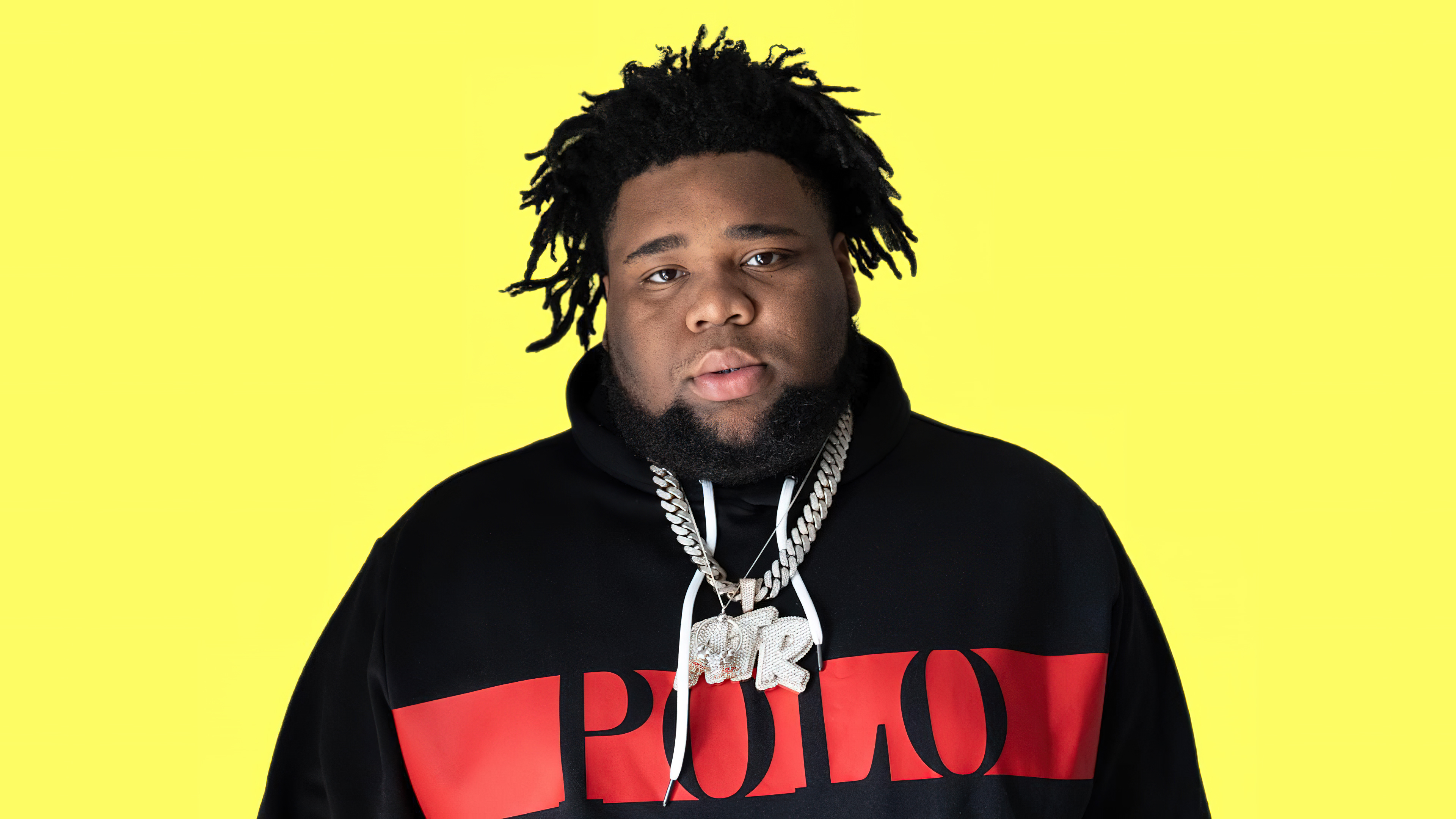 A close-up portrait of American rapper Rod Wave set against a bright yellow background.