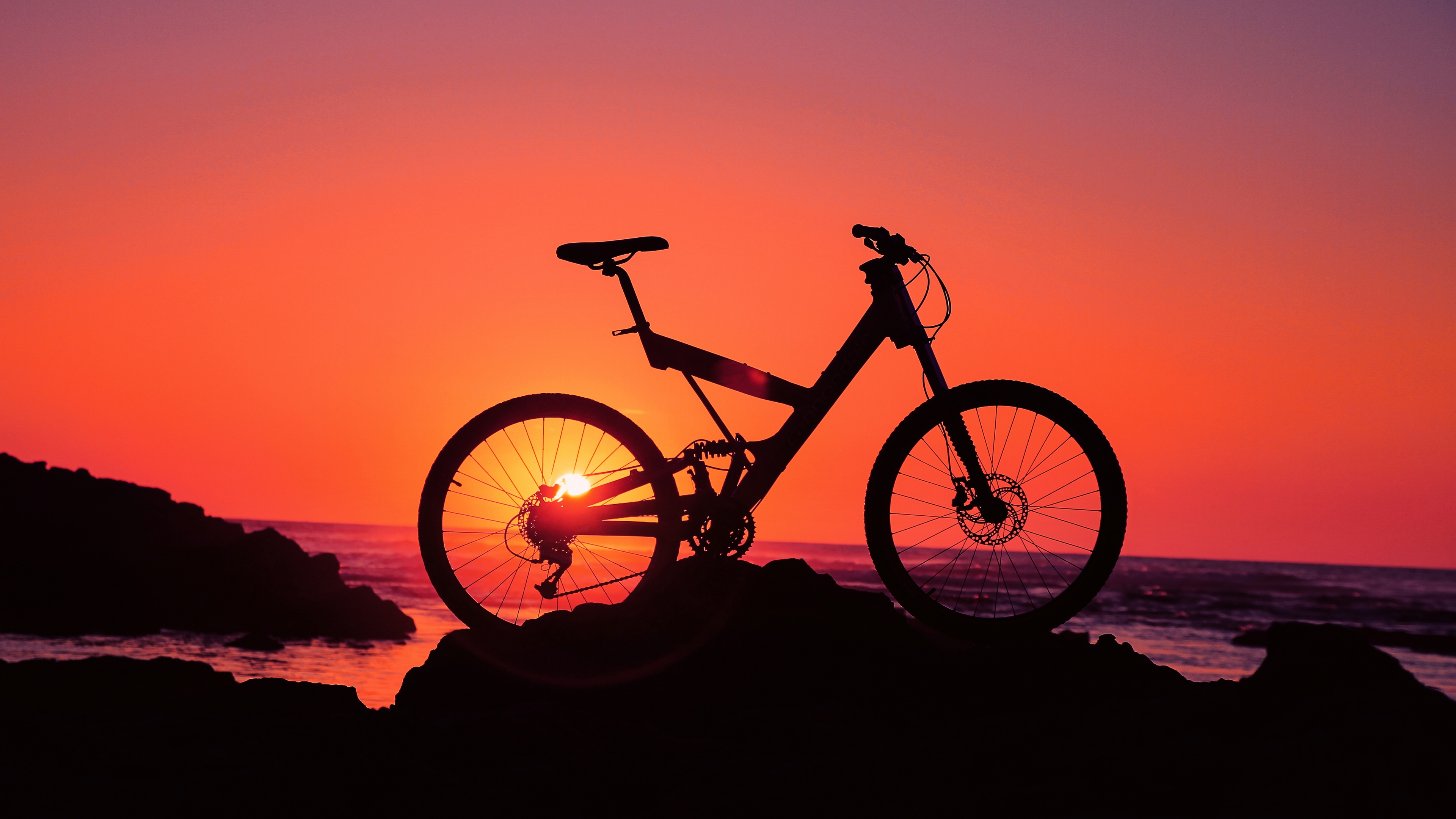 Silhouette of a person riding a bicycle on a beach at sunset in Morocco.