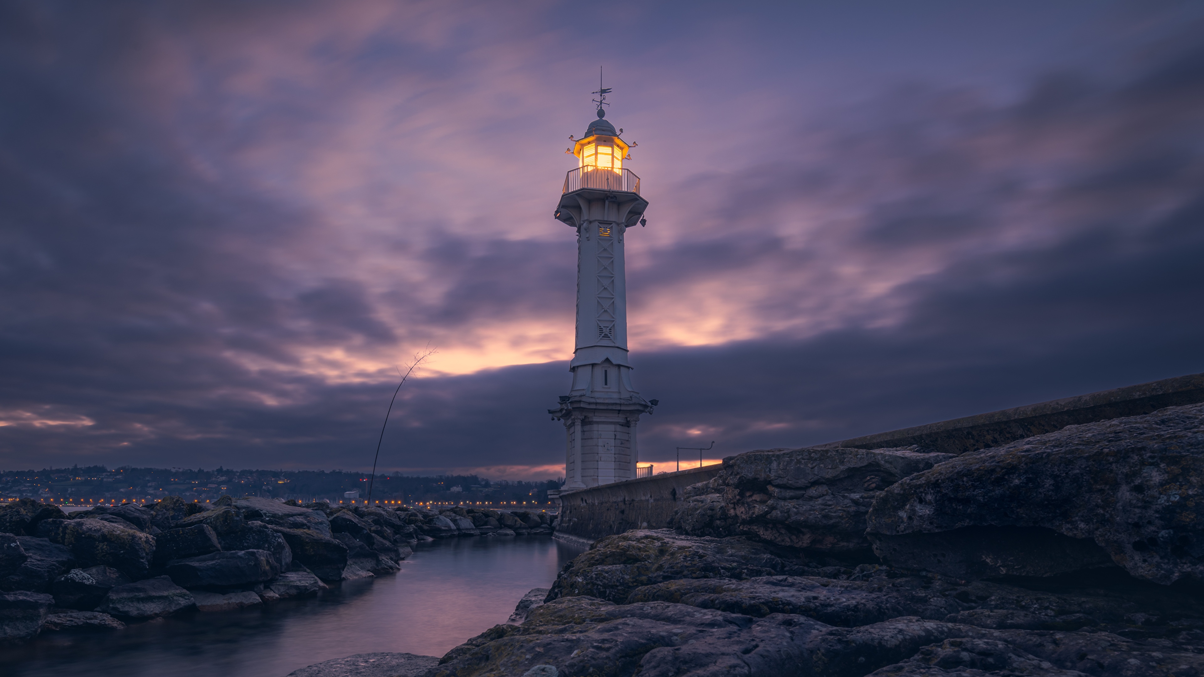 A lighthouse illuminated at dusk in Geneva, Switzerland, with a sunset sky reflecting on the water.