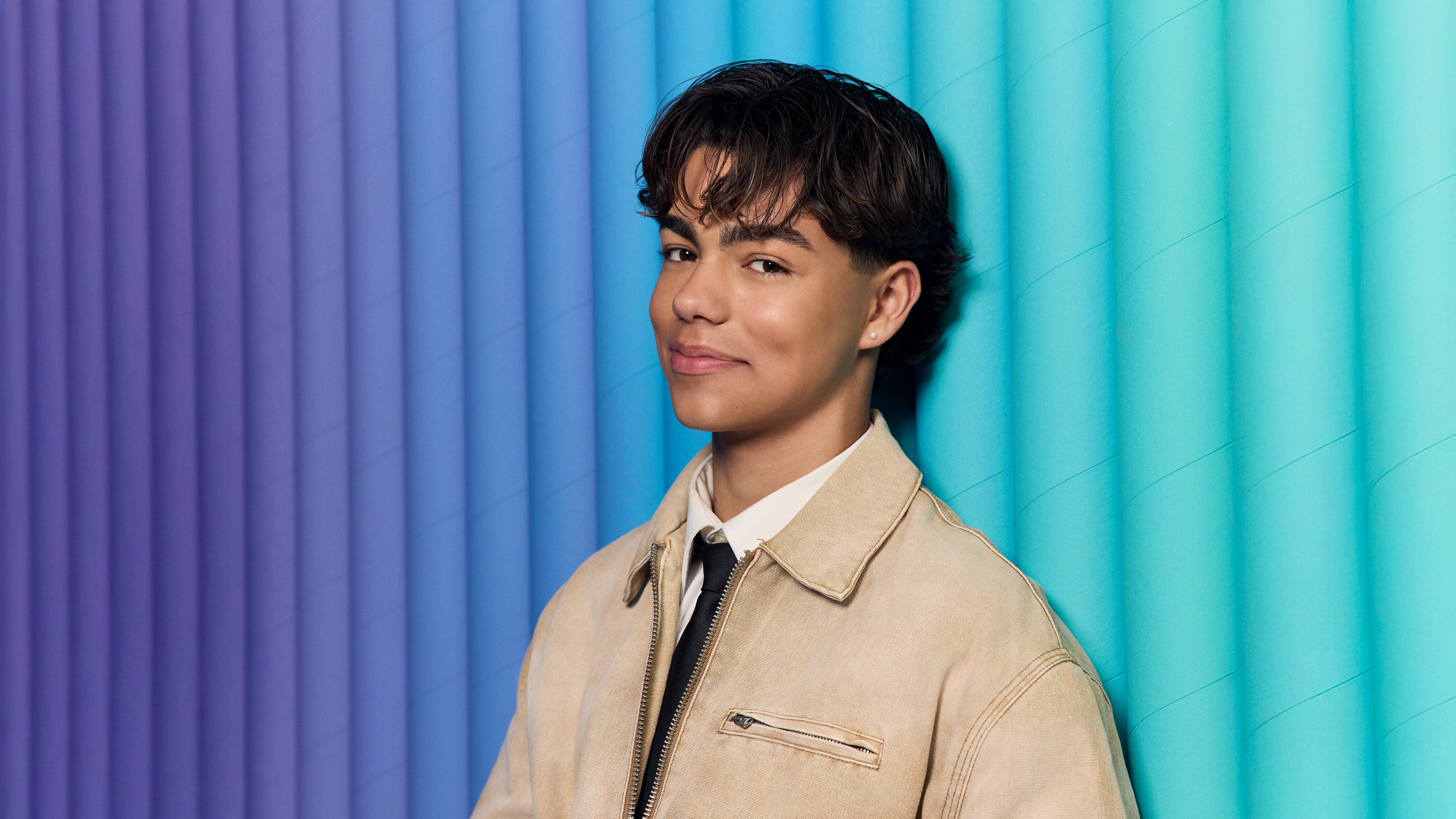 A smiling American actor set against a background of vibrant purple and blue gradient stripes.