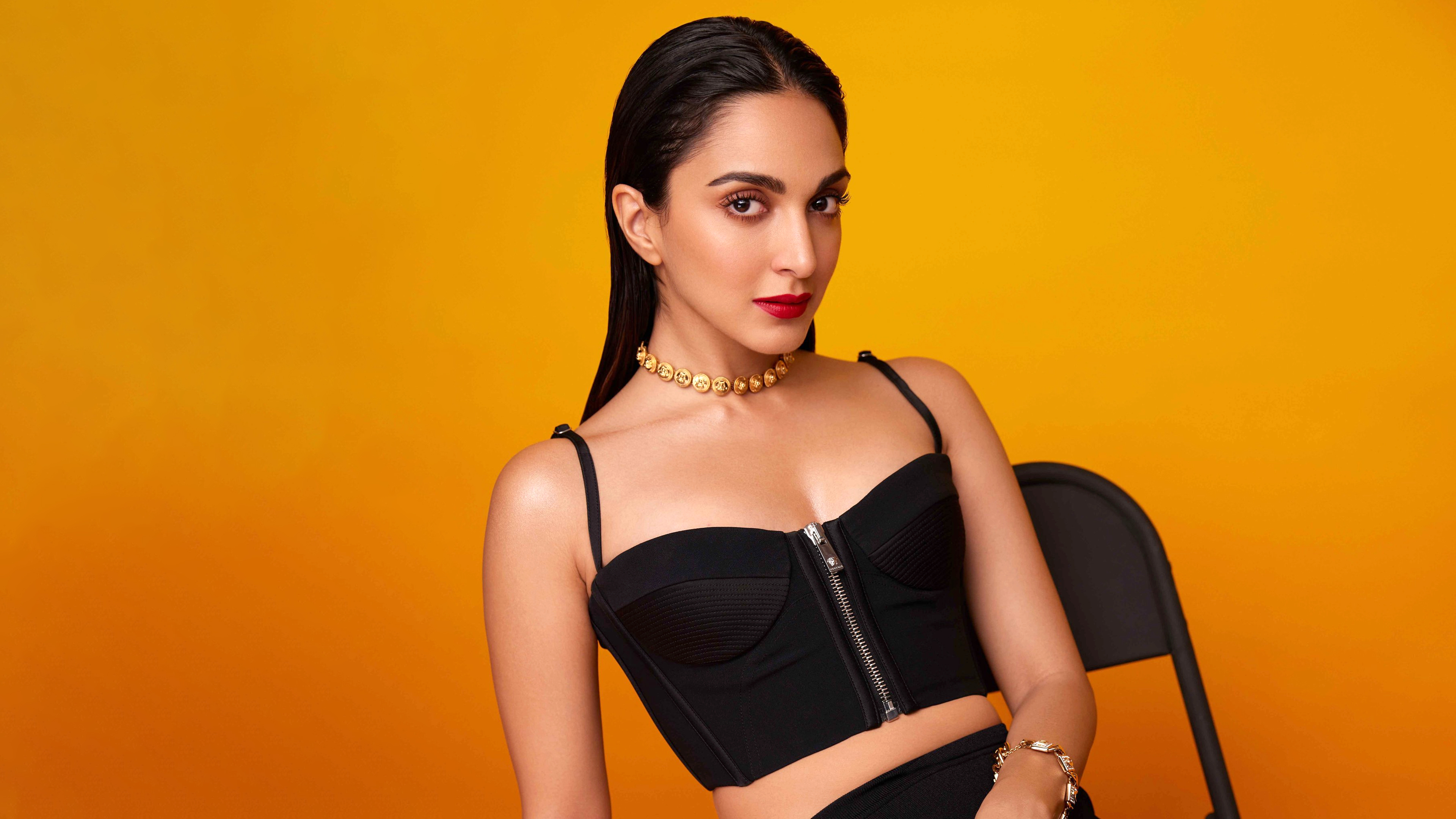 Indian actress Kiara Advani posing in a black dress with an orange background