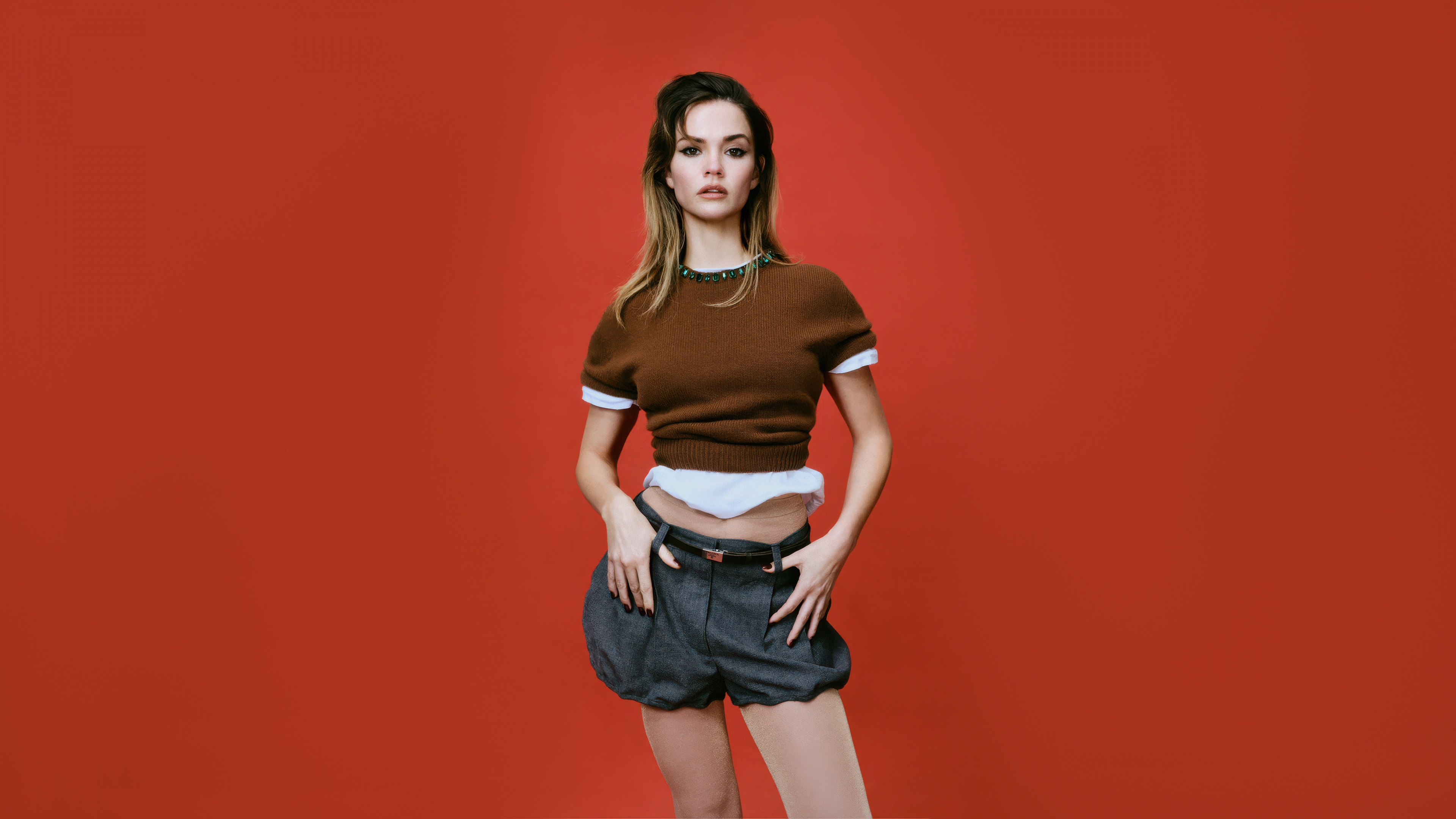 A high-definition portrait of a woman resembling an Australian actress set against a solid, bright orange background.
