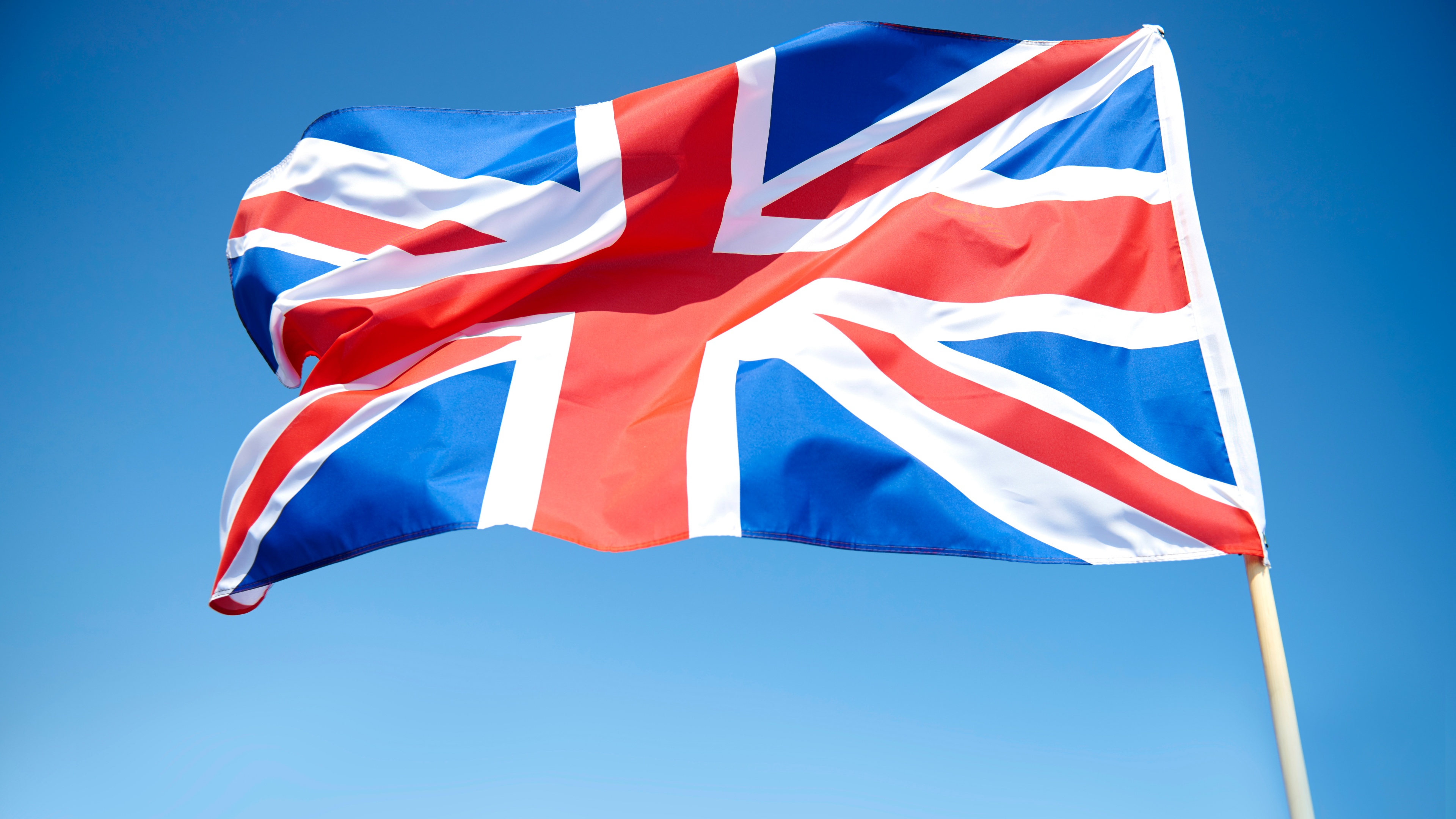 The United Kingdom's Union Jack flag waving against a clear blue sky.