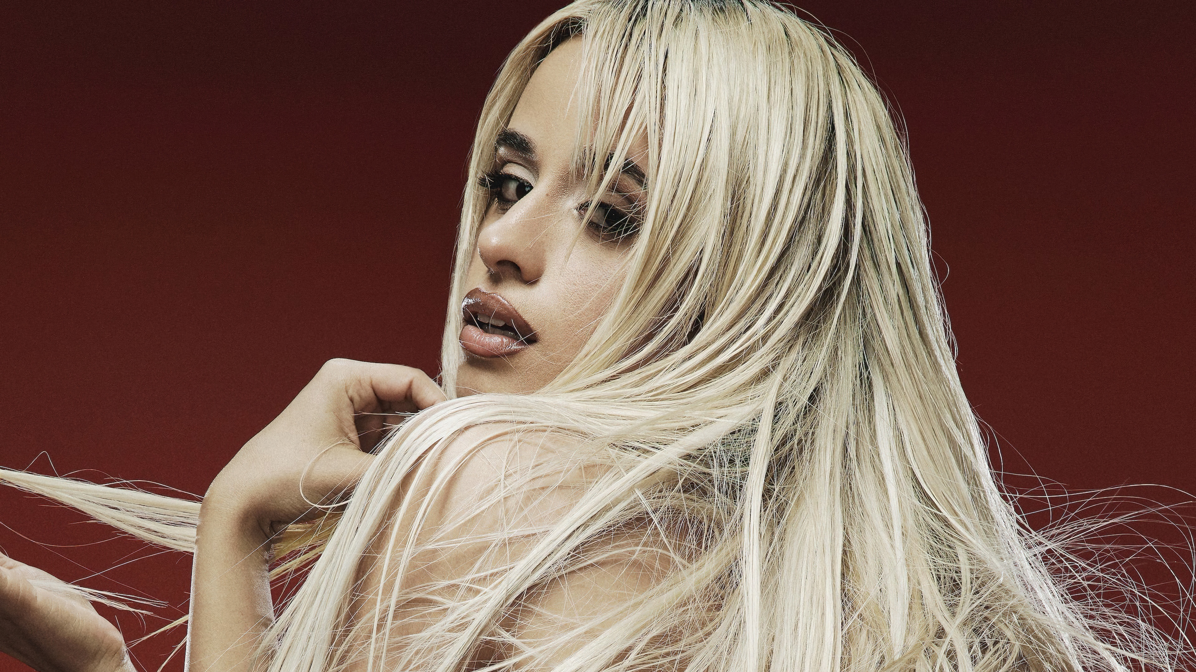A high-contrast portrait of Camila Cabello set against a vivid red background.