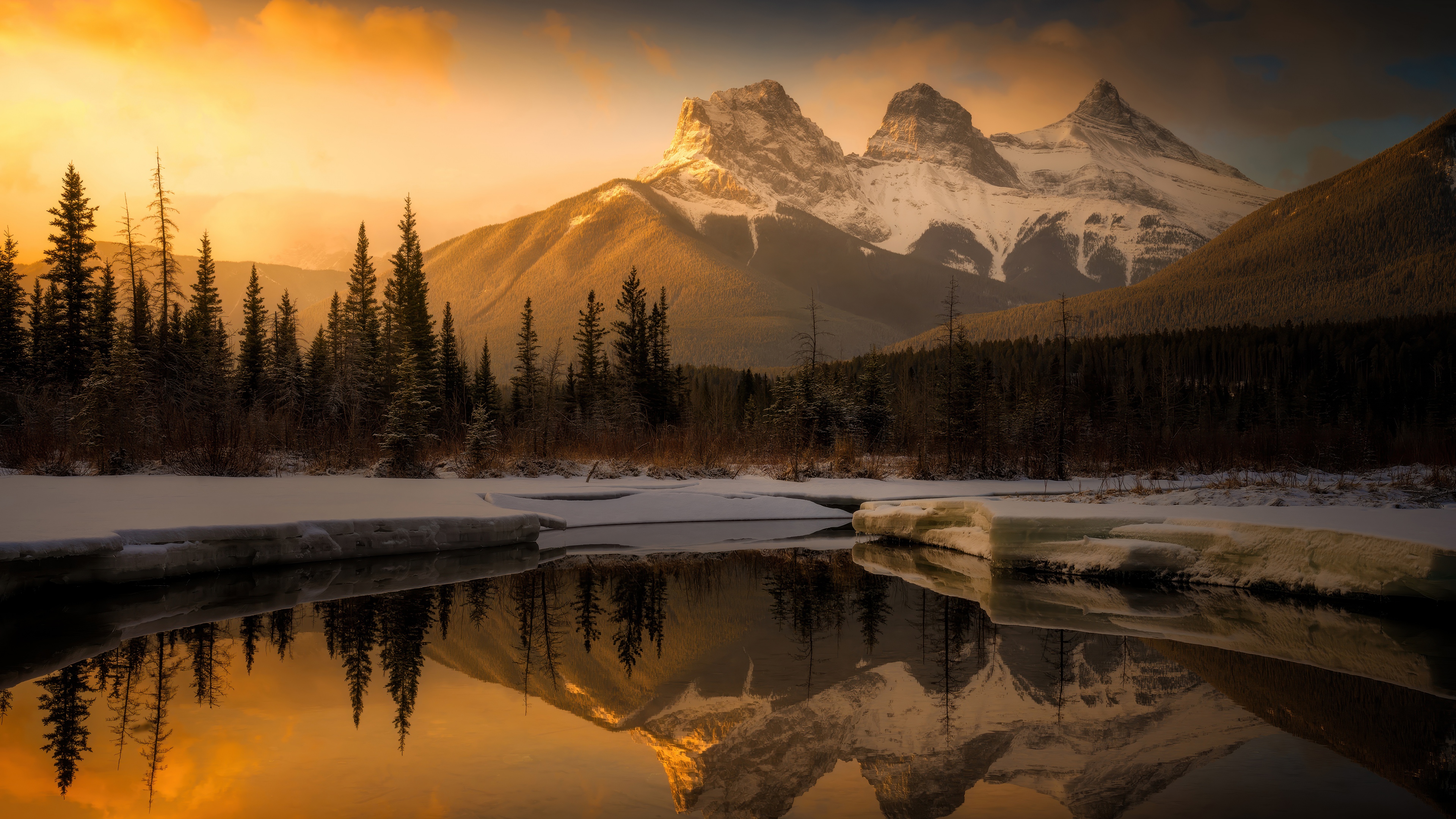 A dramatic sunset over snow-covered mountain peaks in the Oregon wilderness during golden hour.